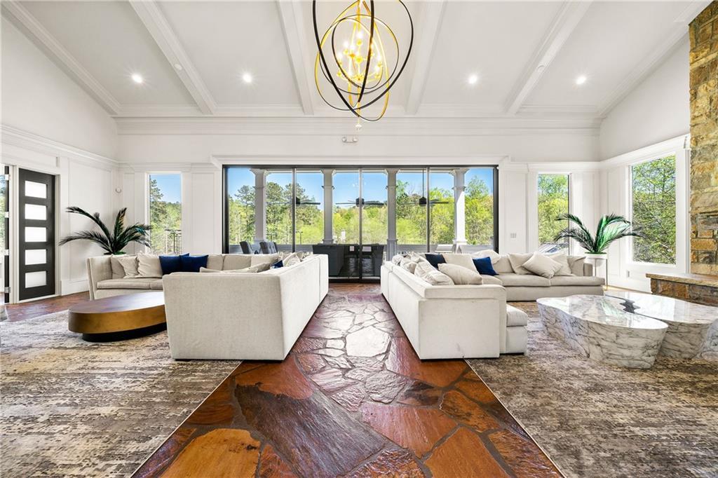 Expansive great room with plush sectional sofas, modern chandelier, stone fireplace, and large windows overlooking greenery in Davidson Homes The Ash B, Riverwood, Dallas, Georgia
