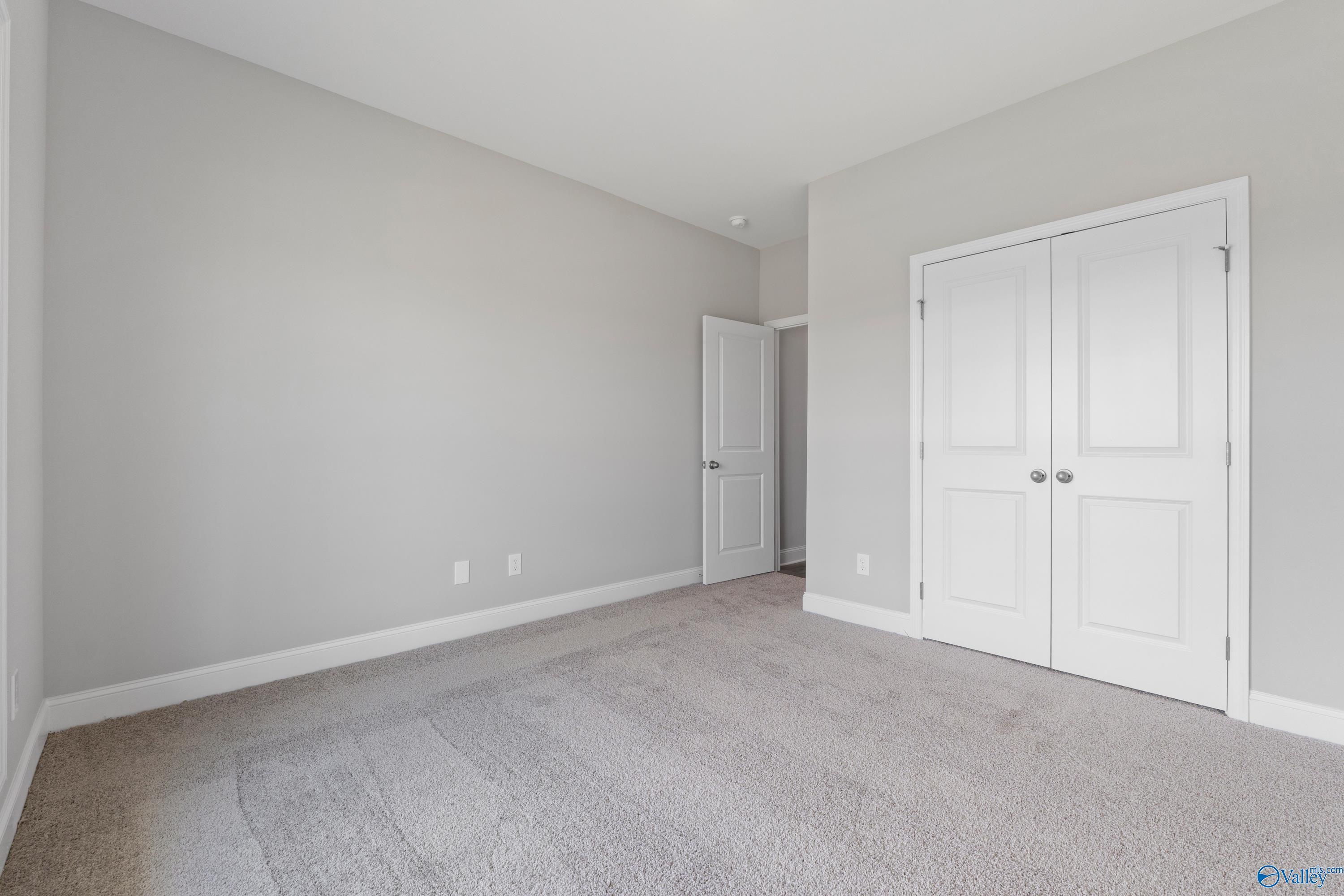 Spacious empty bedroom with gray walls, carpet flooring, and double-door closet in Davidson Homes The Everett B, Toney, Alabama