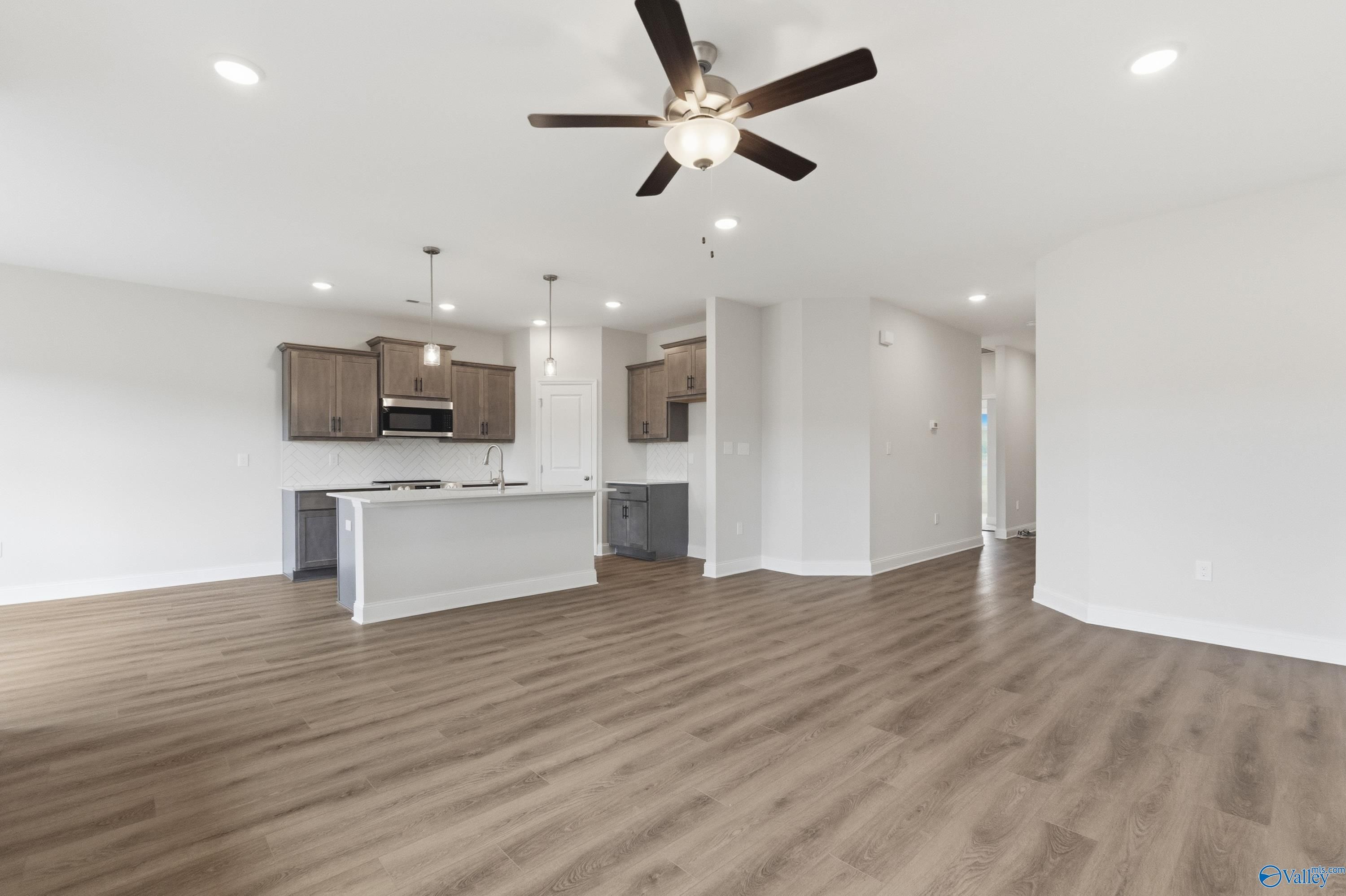 Open-concept kitchen and living space with white island, wood cabinets, and ceiling fan in Davidson Homes The Asheville C, Huntsville, AL