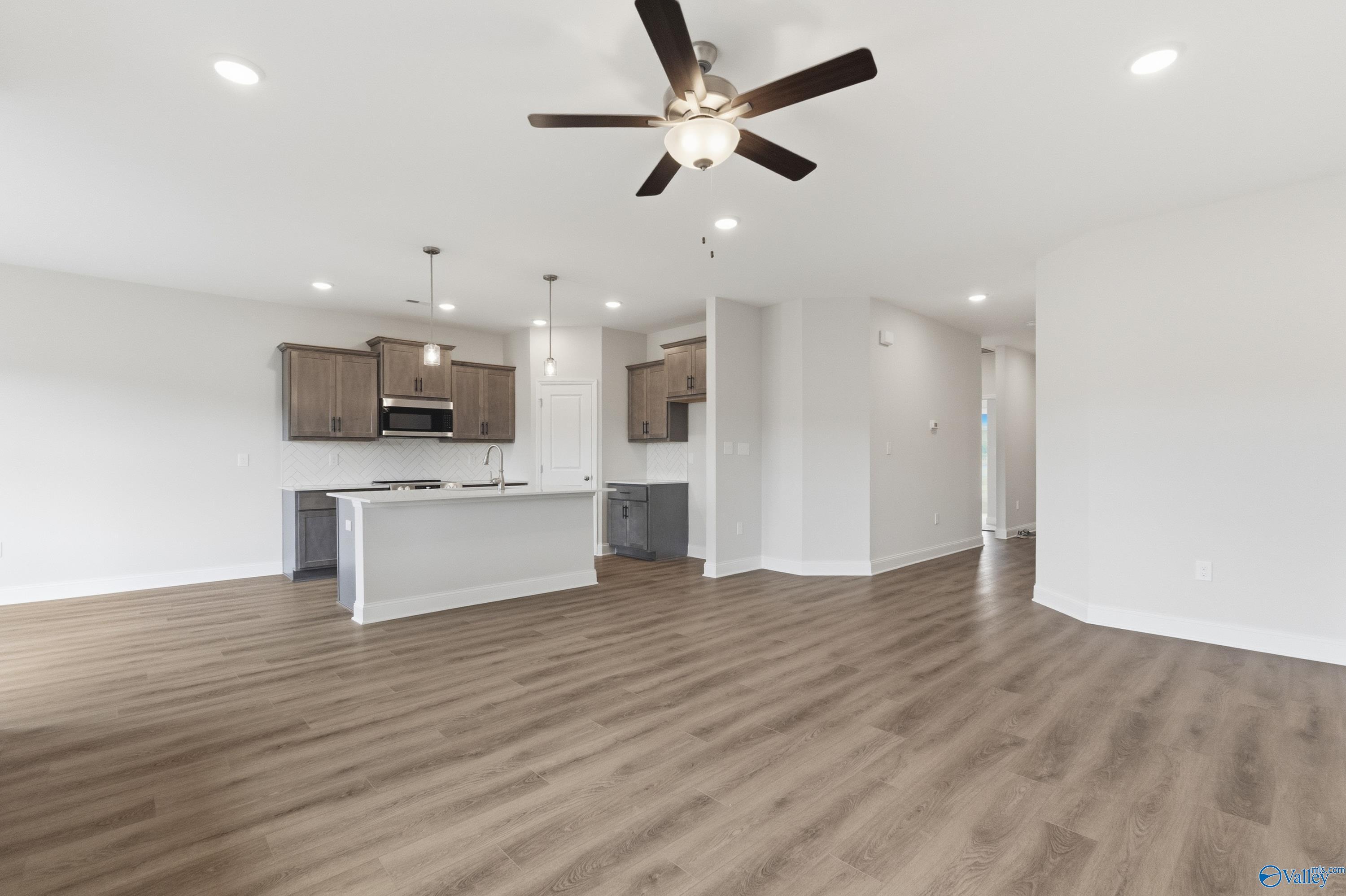Open-concept kitchen and living space with white island, wood cabinets, and ceiling fan in Davidson Homes The Asheville C, Huntsville, AL