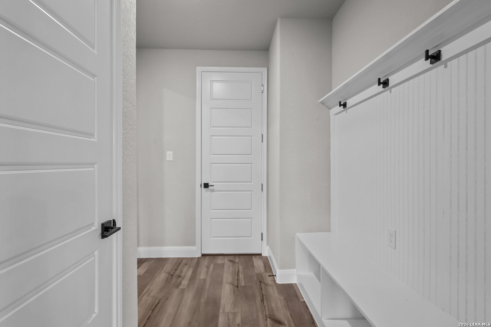 Bright mudroom entry with white beadboard hooks, built-in bench, hardwood floors in Davidson Homes The Belmont H, Castroville, Texas