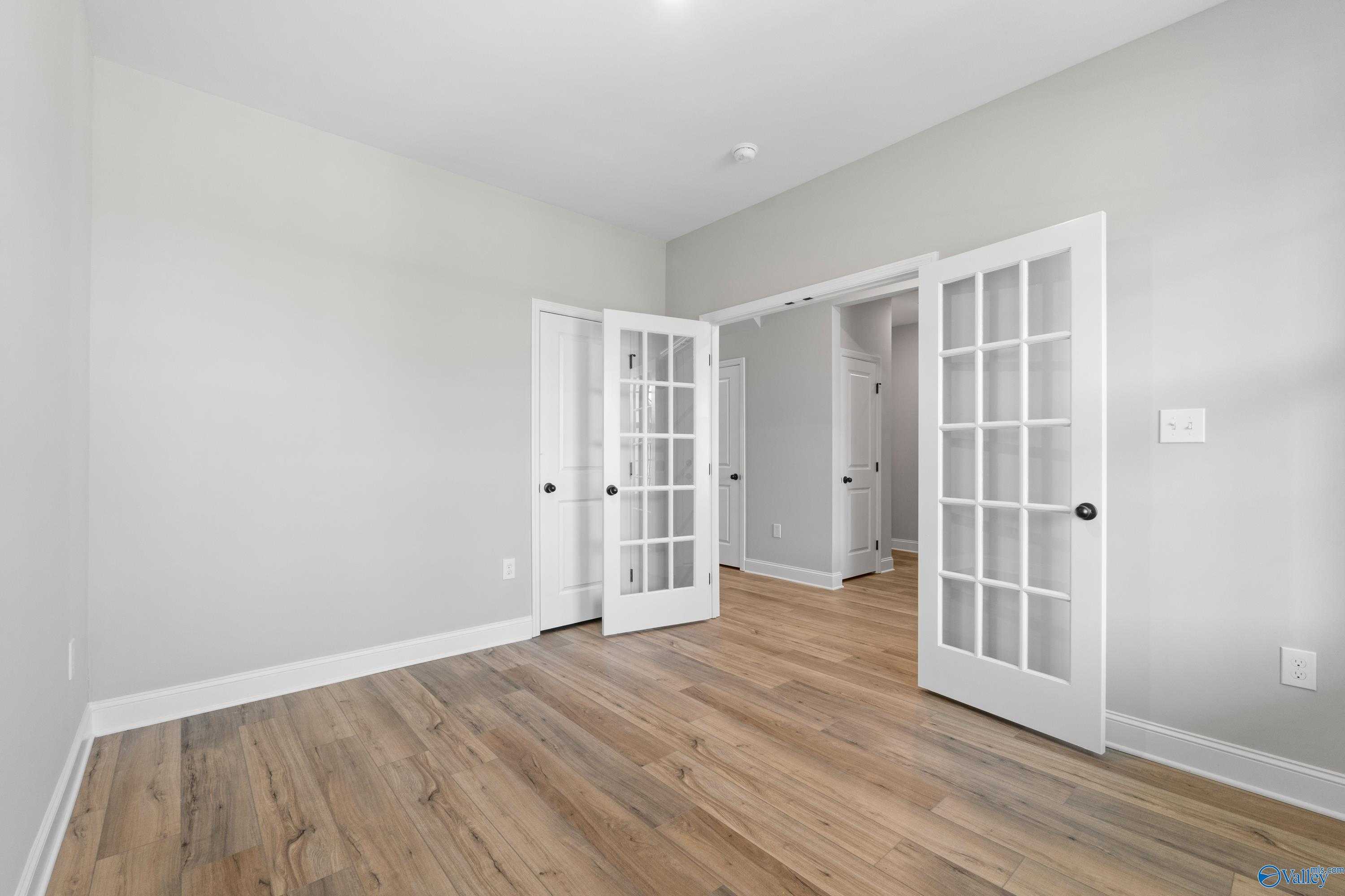 Bonus room featuring light gray walls, oak hardwood floors, and white French doors in Davidson Homes The Rockford with Bonus, Toney, AL