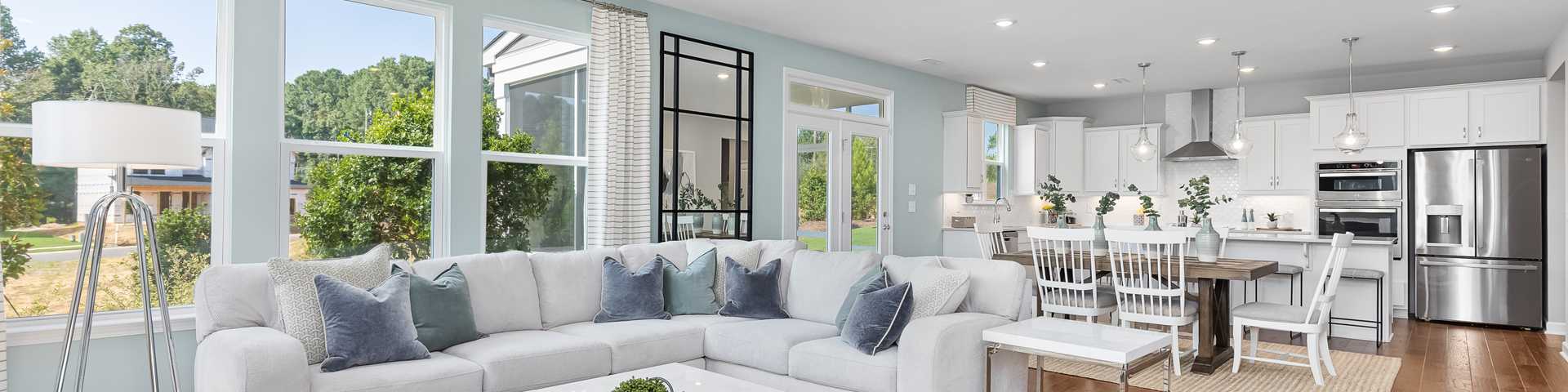 Spacious open-concept living room and kitchen in new Lillington home, white L-shaped sofa, wood floors, large windows