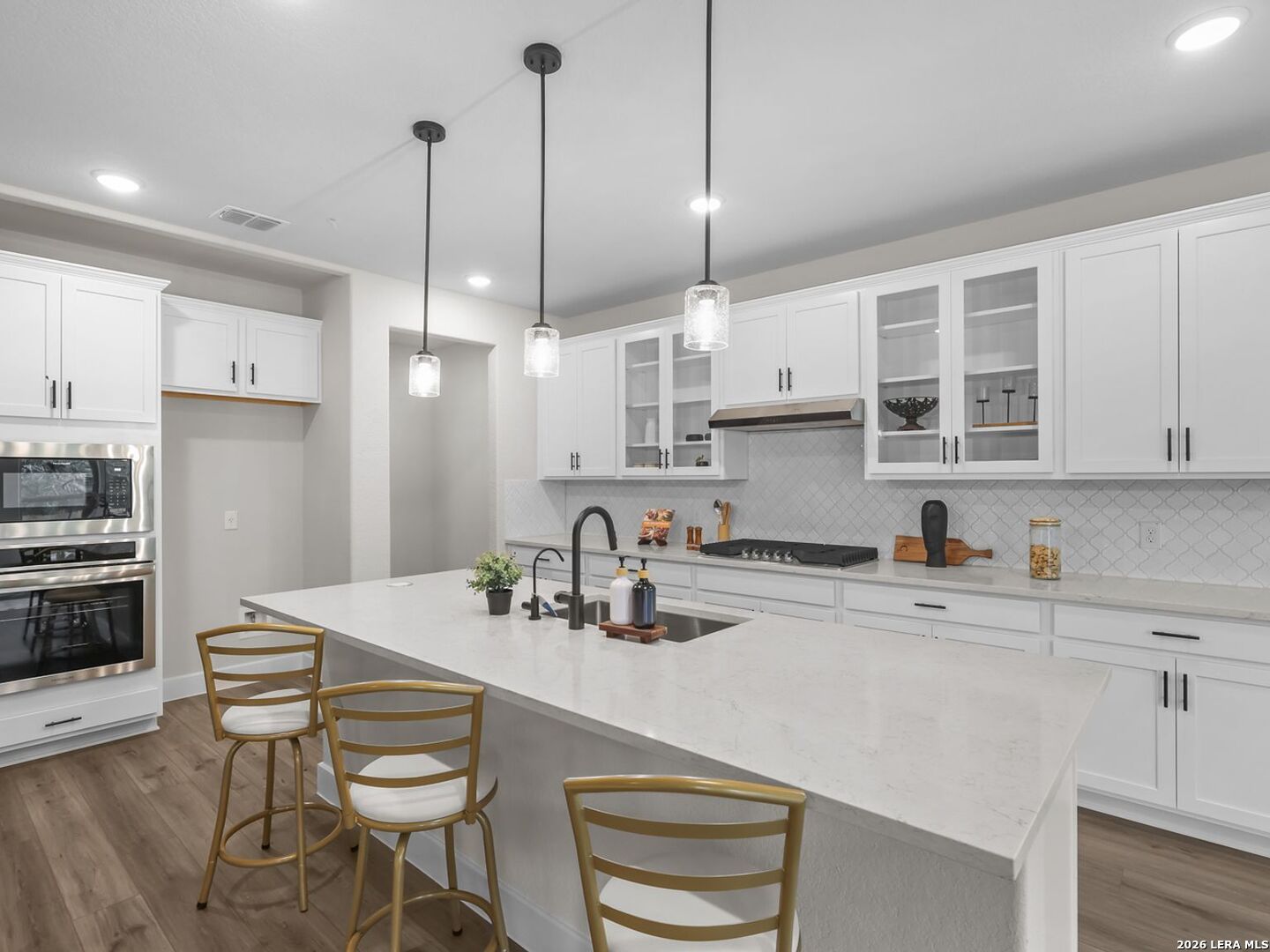 Modern kitchen with white cabinets, quartz island, and gold bar stools in The Belmont H home in Potranco Oaks, Castroville.