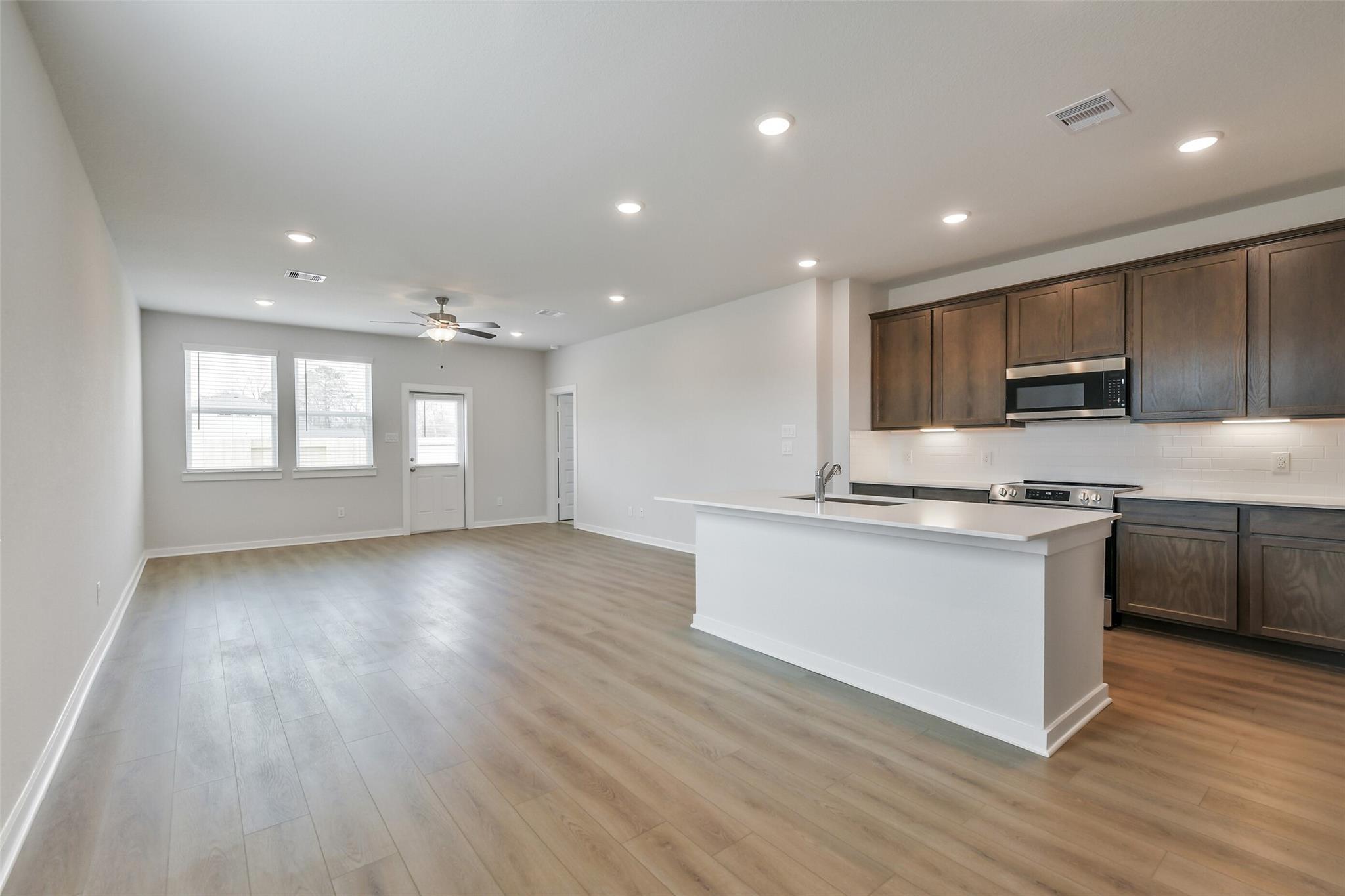 Modern open-concept kitchen with white island, stainless appliances, and hardwood floors in The Brazos E, Cleveland, Texas