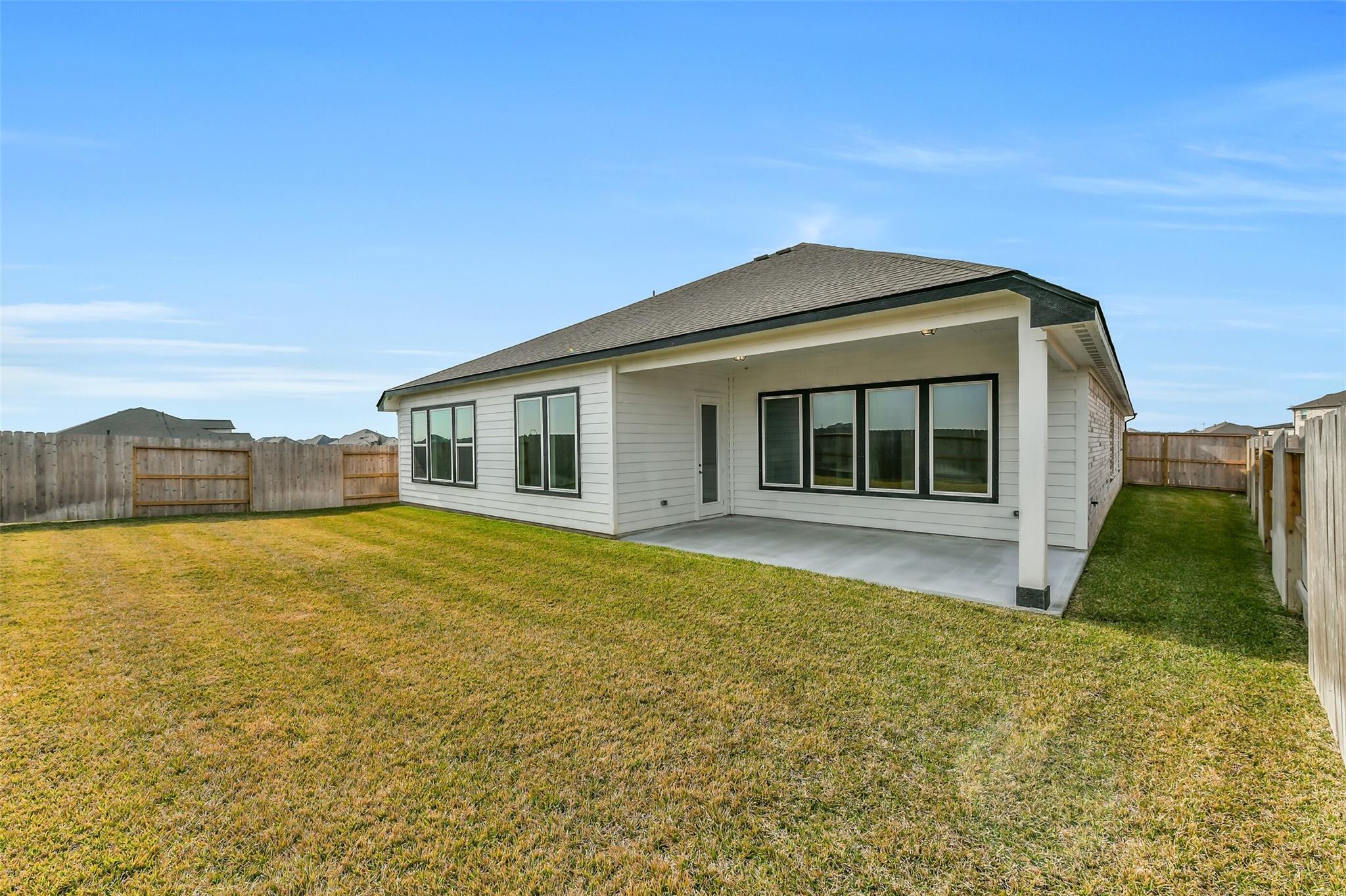 Modern 1-story home rear view featuring covered patio, large windows, and grassy backyard in Lago Mar, Texas City - The George A by Davidson Homes