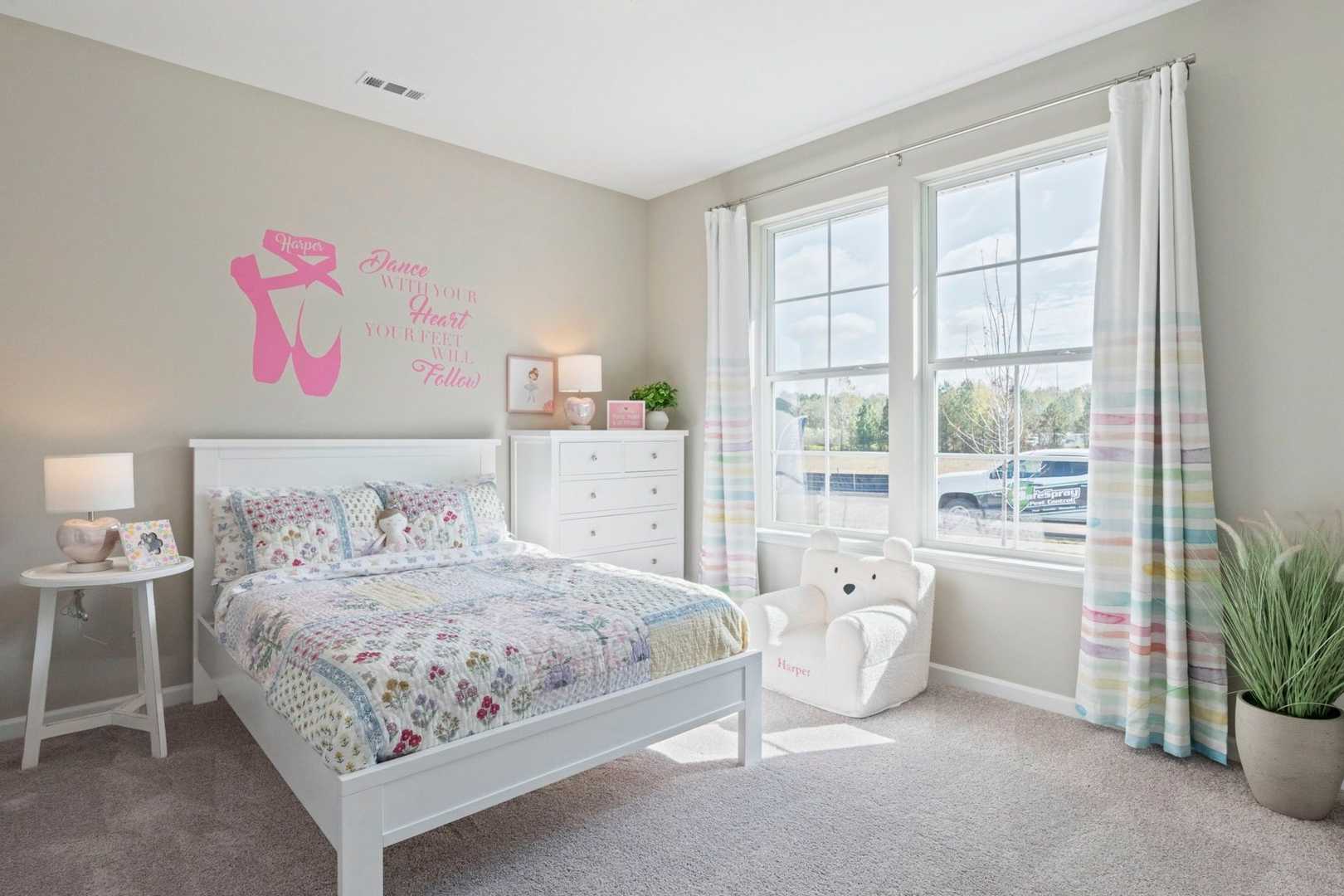 Cozy girl's bedroom in The Phoenix by Evermore Homes featuring pink ballet wall decal, white bed with quilt, and large windows