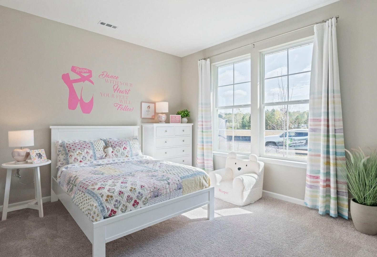 Charming ballet-themed girl's bedroom in The Phoenix A by Davidson Homes, white bed with quilt, dresser, teddy bear chair, large windows