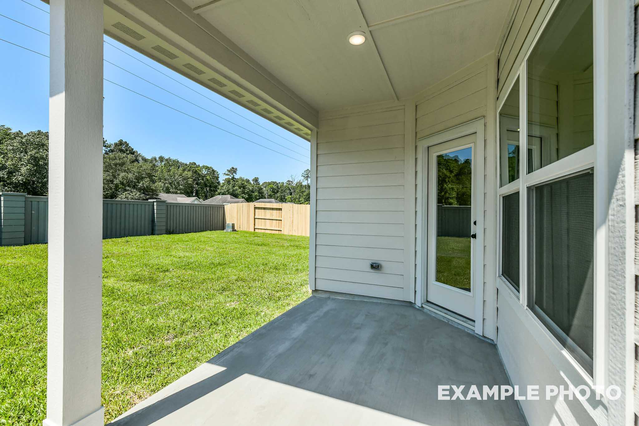 Covered patio of The Daphne G home design featuring glass door, white siding exterior, and lush green backyard