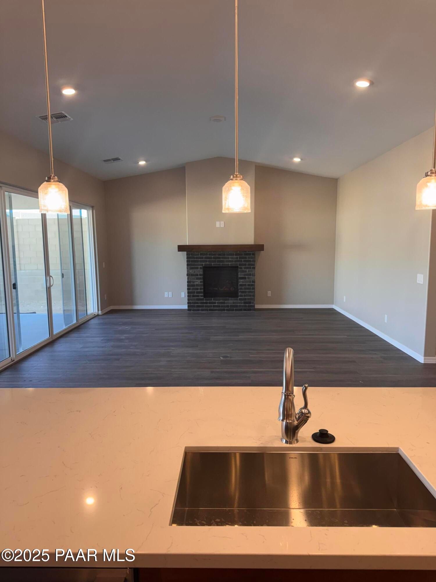 Open-concept kitchen island with quartz countertop, stainless sink, brick fireplace, and sliding doors in Davidson Homes Sunrise II A, Prescott AZ