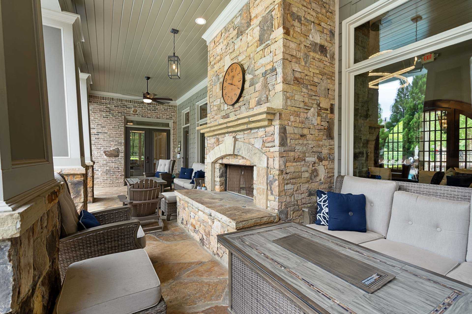 Cozy covered patio with stone fireplace at The Village at Towne Lake in Woodstock Georgia featuring wicker seating and ceiling fan
