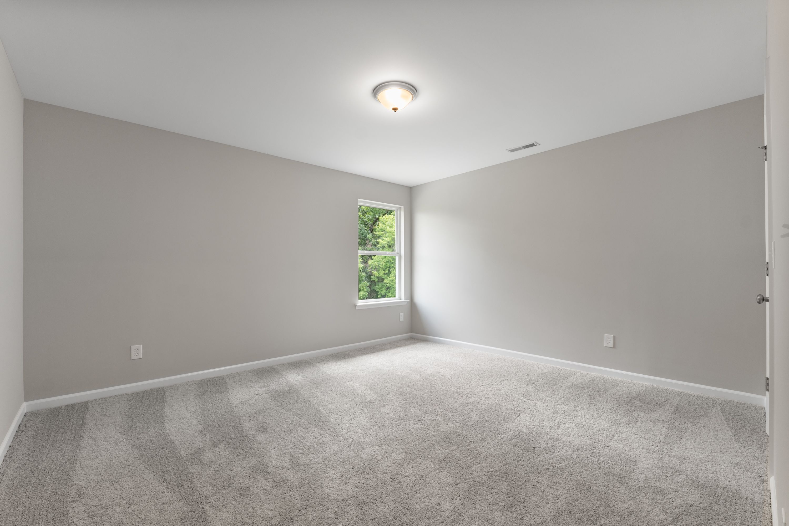 Spacious empty bedroom in The Avalon E with light gray walls, berber carpet, large window, and flush ceiling light