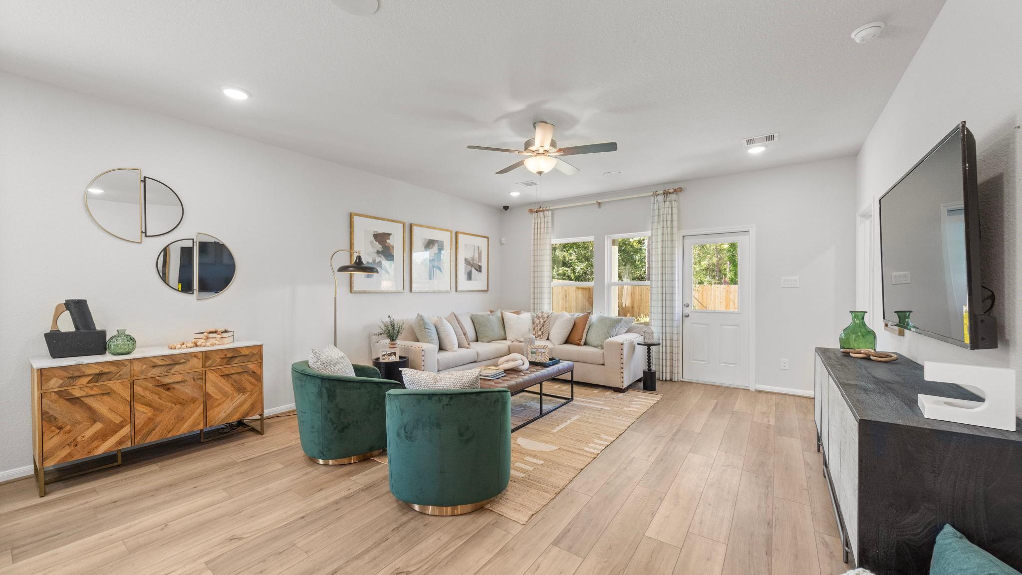 Spacious modern living room at Robins Landing in Houston TX with hardwood floors, green velvet armchairs, beige sectional sofa, and large windows