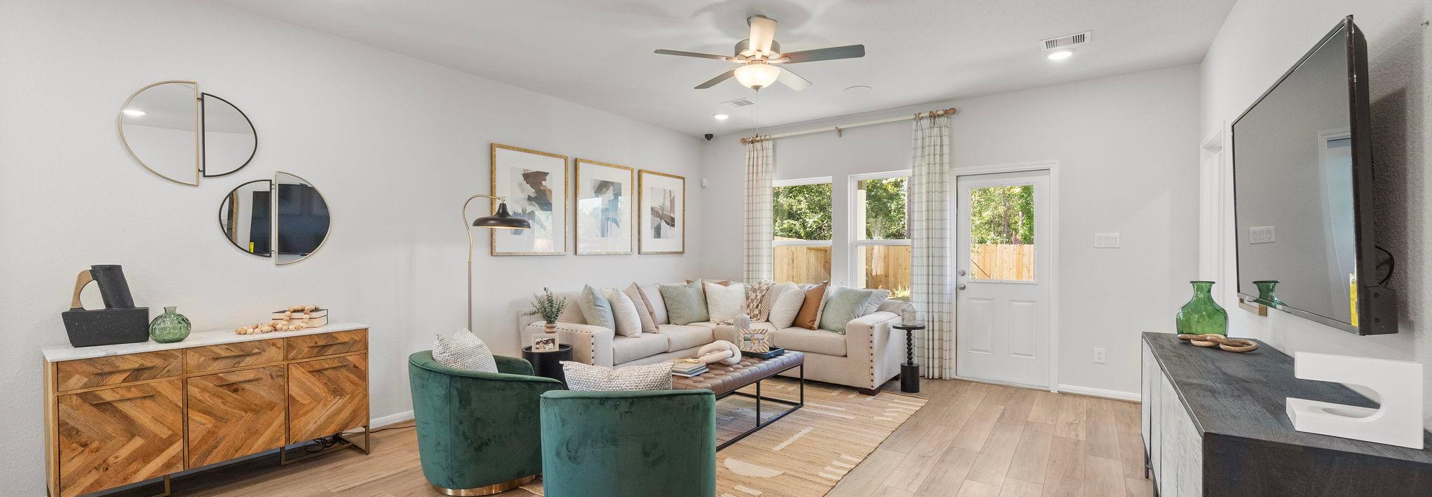 Spacious modern living room at Robins Landing in Houston TX with hardwood floors, green velvet armchairs, beige sectional sofa, and large windows