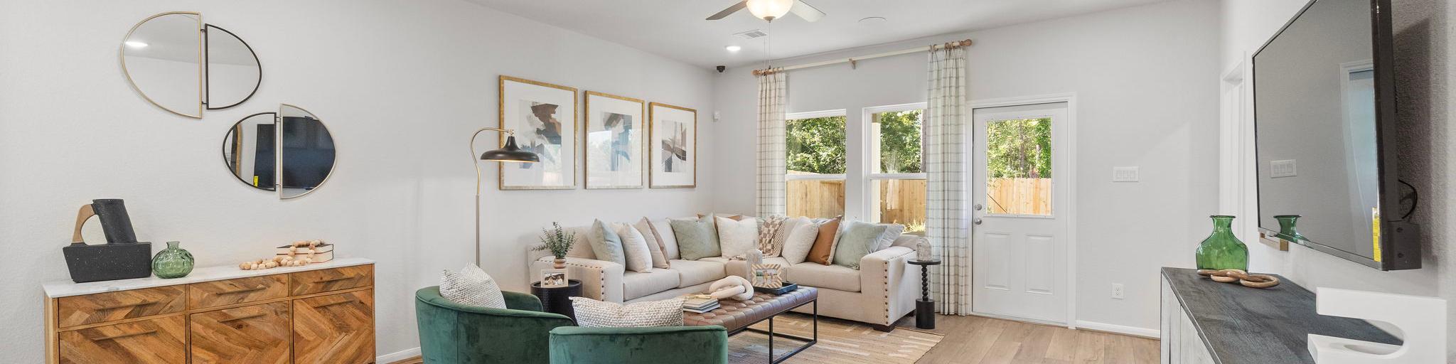 Spacious modern living room at Robins Landing in Houston TX with hardwood floors, green velvet armchairs, beige sectional sofa, and large windows