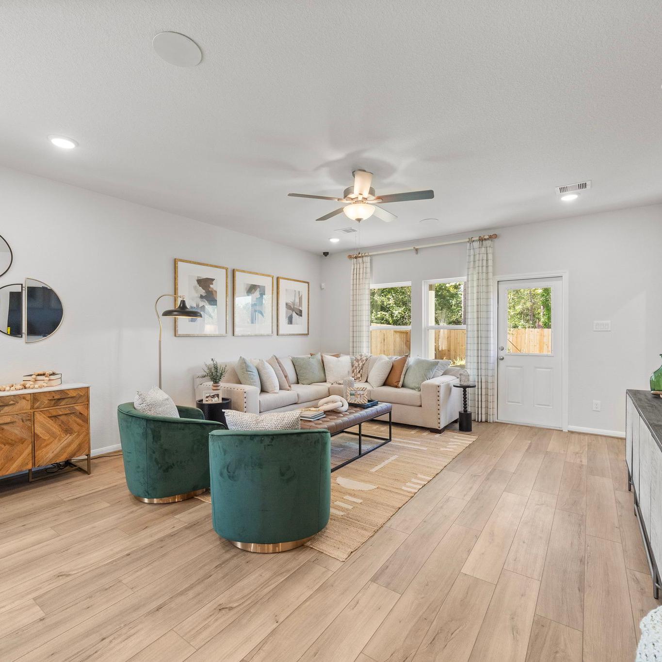 Spacious modern living room at Robins Landing in Houston TX with hardwood floors, green velvet armchairs, beige sectional sofa, and large windows