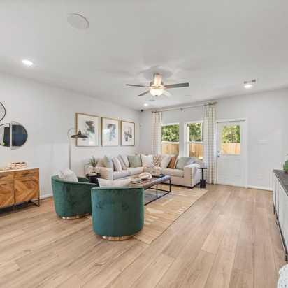 Spacious modern living room at Robins Landing in Houston TX with hardwood floors, green velvet armchairs, beige sectional sofa, and large windows