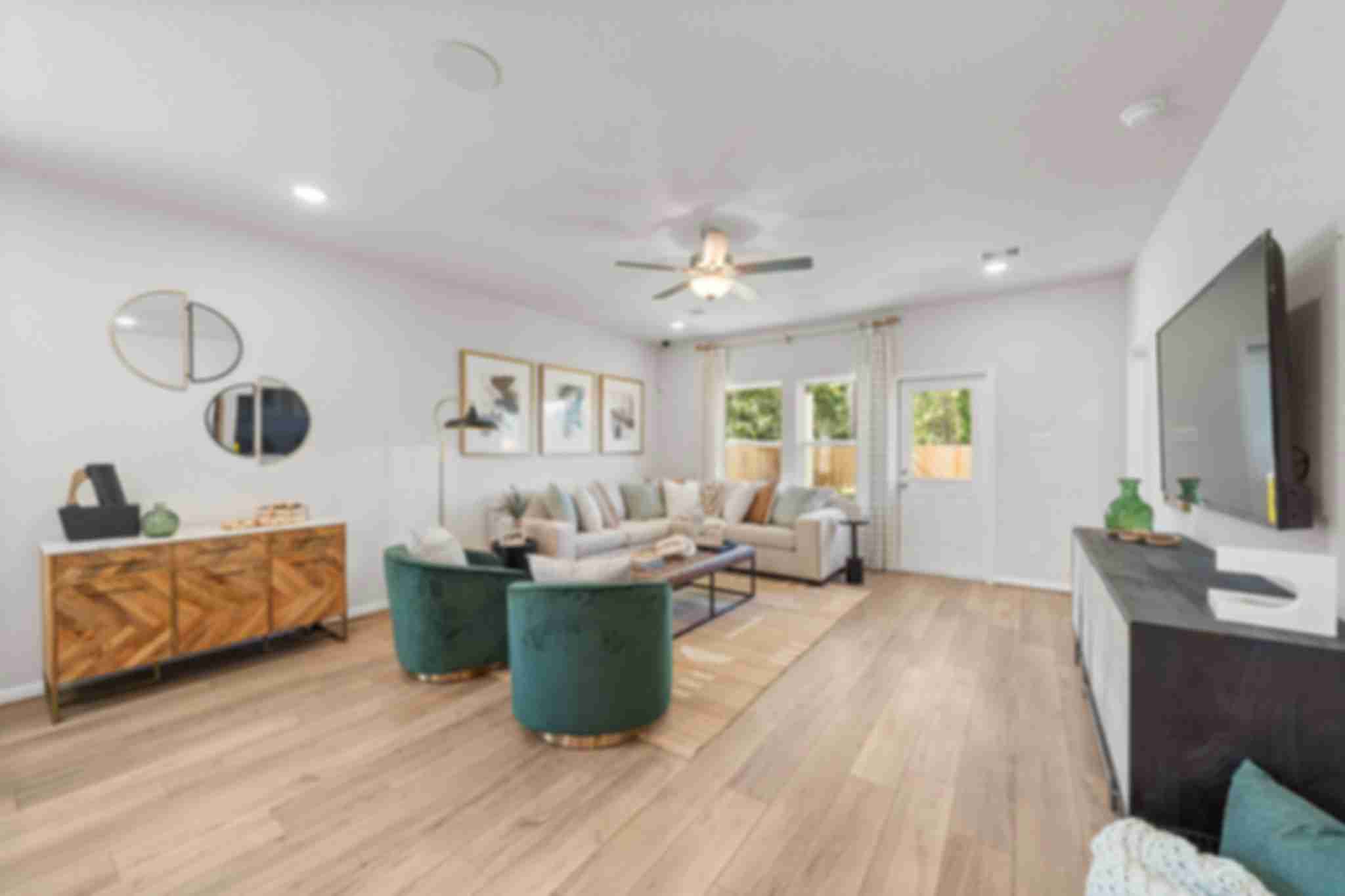 Spacious modern living room at Robins Landing in Houston TX with hardwood floors, green velvet armchairs, beige sectional sofa, and large windows