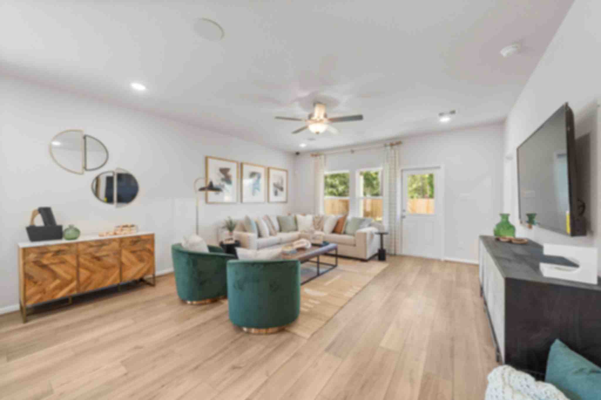 Spacious modern living room at Robins Landing in Houston TX with hardwood floors, green velvet armchairs, beige sectional sofa, and large windows