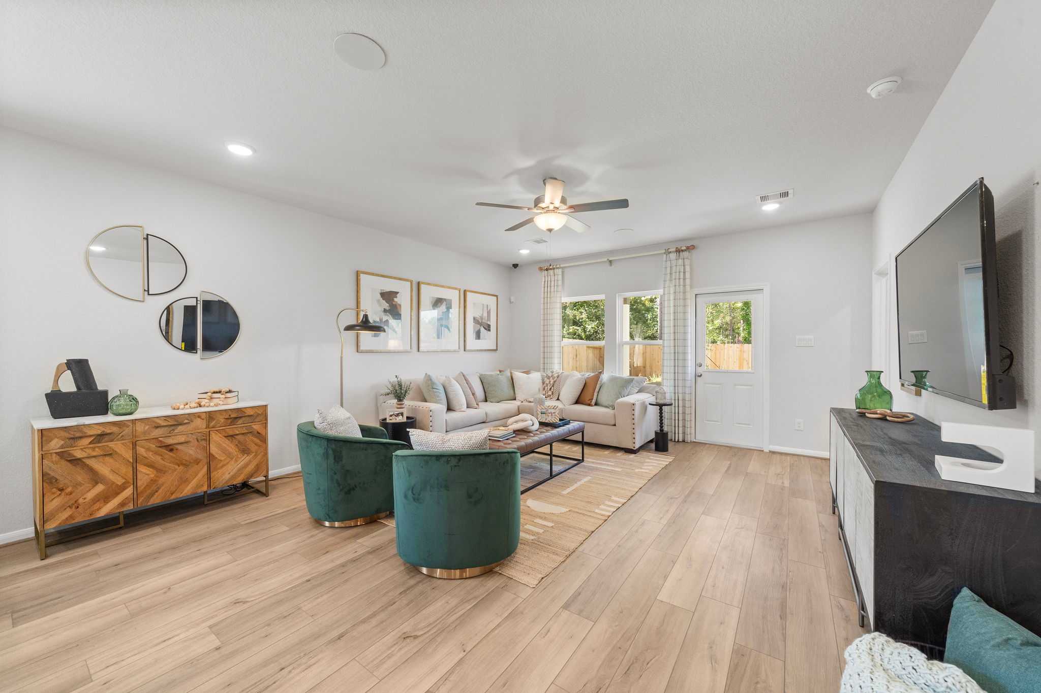 Spacious living room at Caney Creek Place in Conroe Texas with hardwood floors, green velvet armchairs, beige sofa, and wall TV
