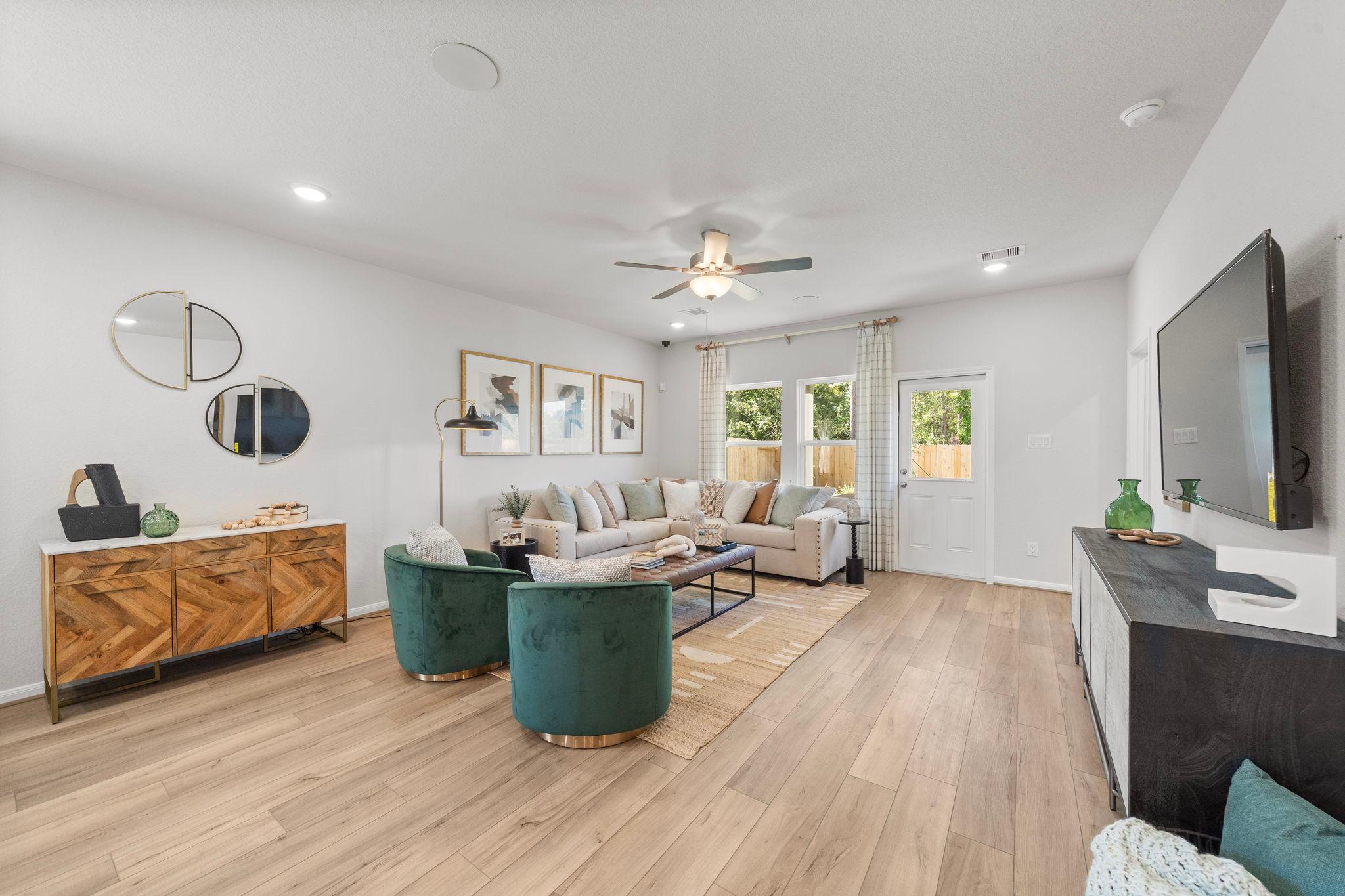 Spacious living room at Caney Creek Place in Conroe Texas with hardwood floors, green velvet armchairs, beige sofa, and wall TV