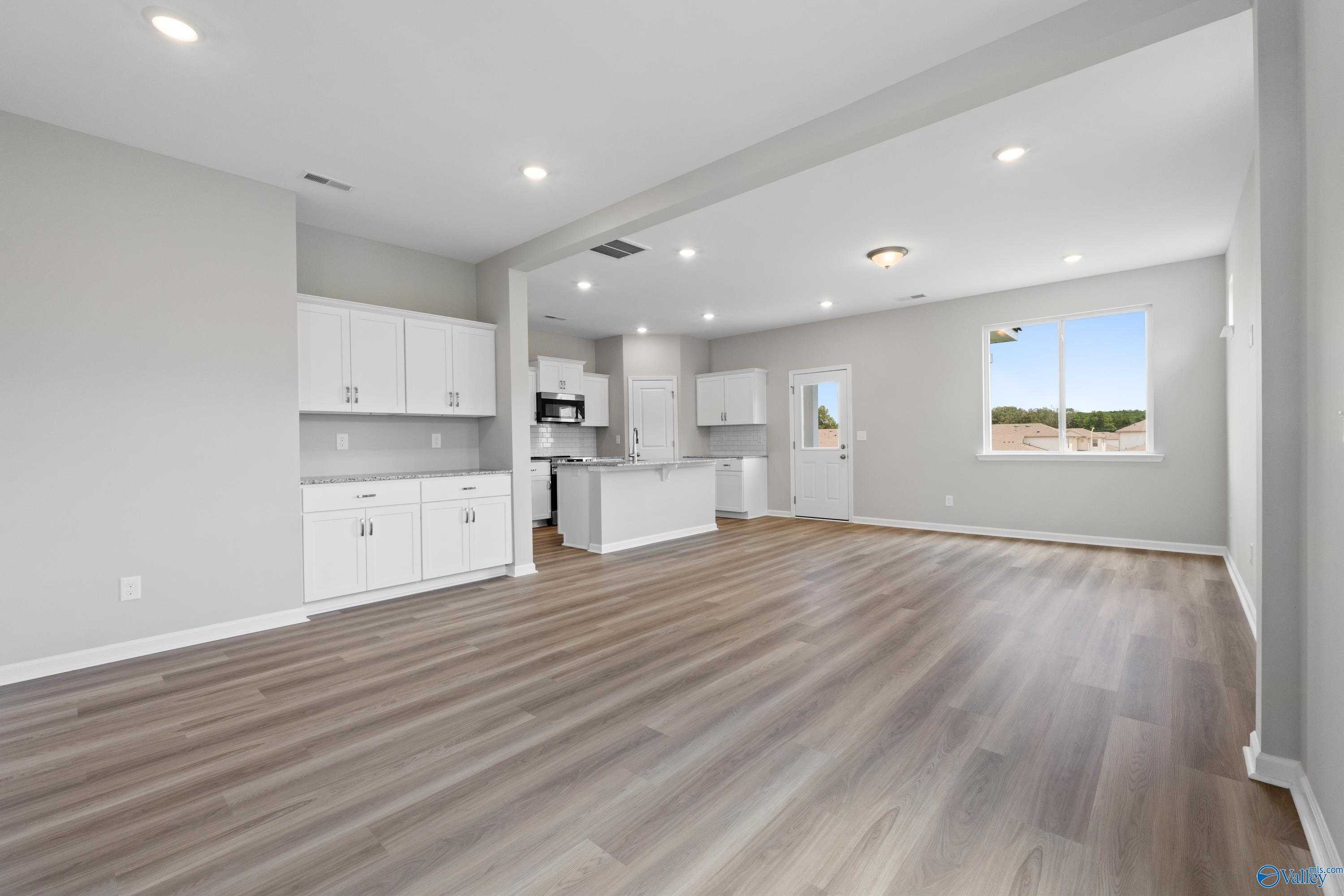 Modern open kitchen with white cabinets, center island, hardwood floors in Evermore Homes The Augusta, Madison, Alabama
