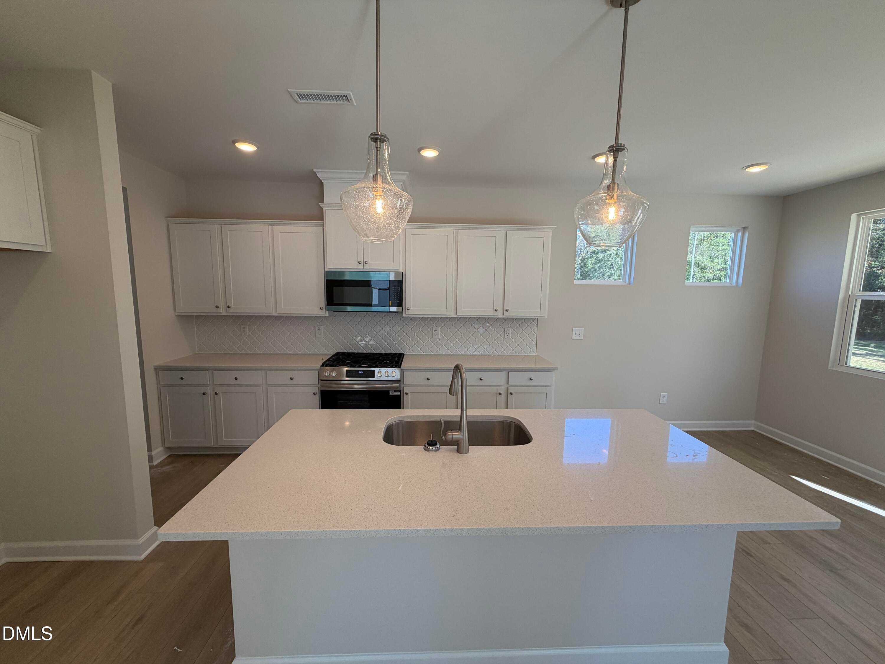 Bright open-concept kitchen with white cabinets, quartz island sink, stainless appliances and pendant lights in The Gavin C, Lillington, NC