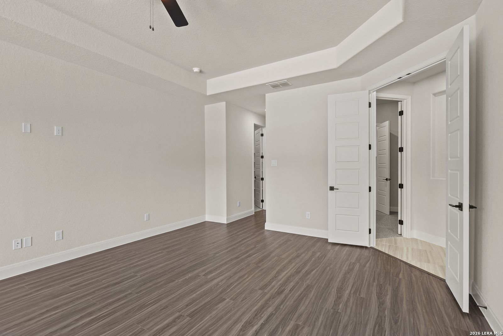 Spacious bedroom with tray ceiling and wood-style flooring in The Summerlin B floor plan at Potranco Oaks, Castroville, TX.