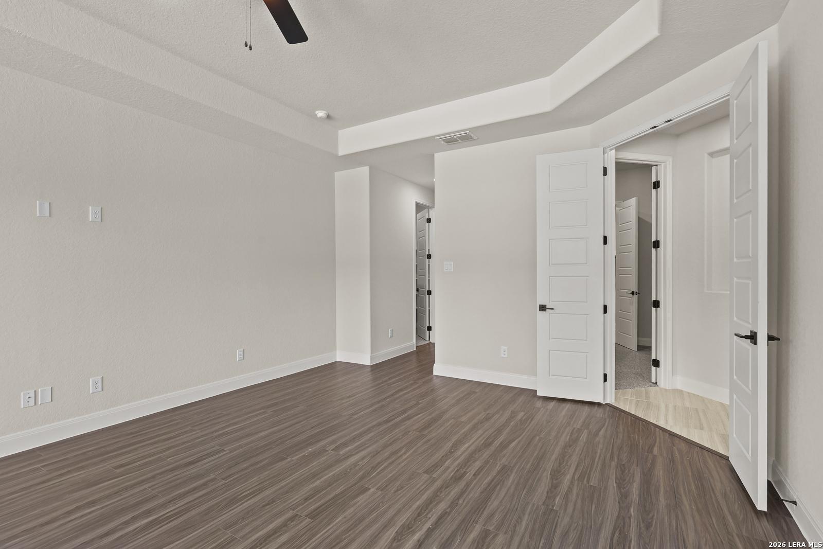 Spacious bedroom with tray ceiling and wood-style flooring in The Summerlin B floor plan at Potranco Oaks, Castroville, TX.