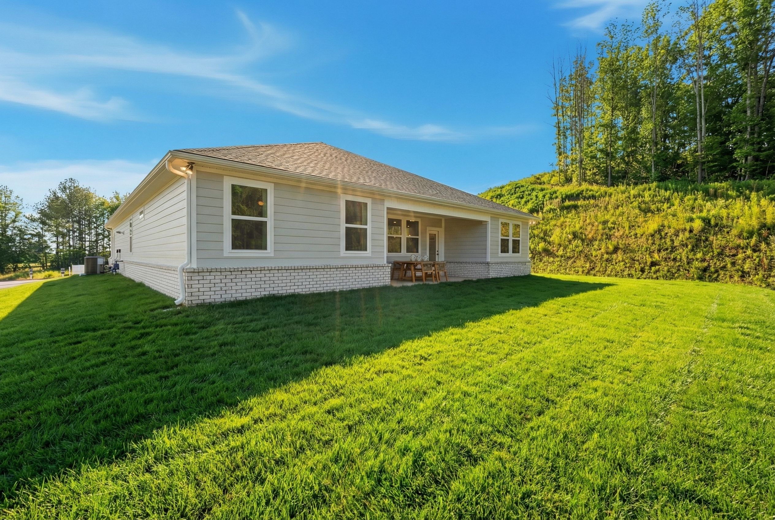 Ranch-style home exterior at Noble Ridge in Cullman Alabama with covered porch, white siding, green lawn and wooded hillside