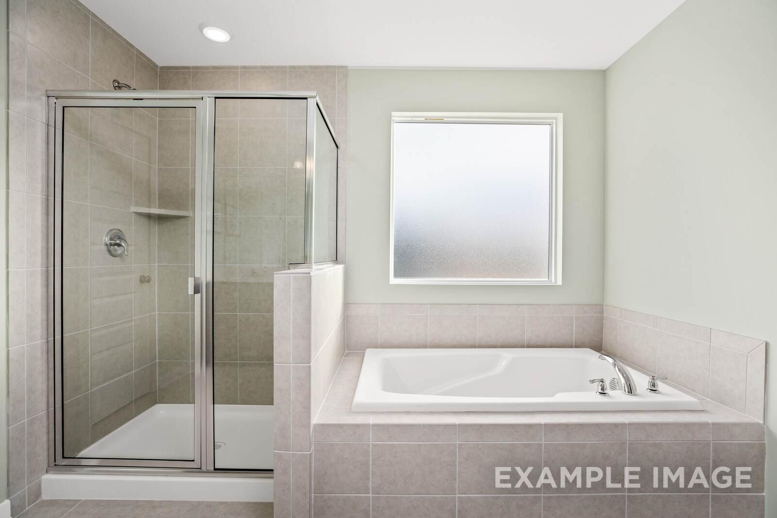 Spacious master bathroom in The Gordon C with frameless glass shower, soaking tub, neutral tiles, and frosted window
