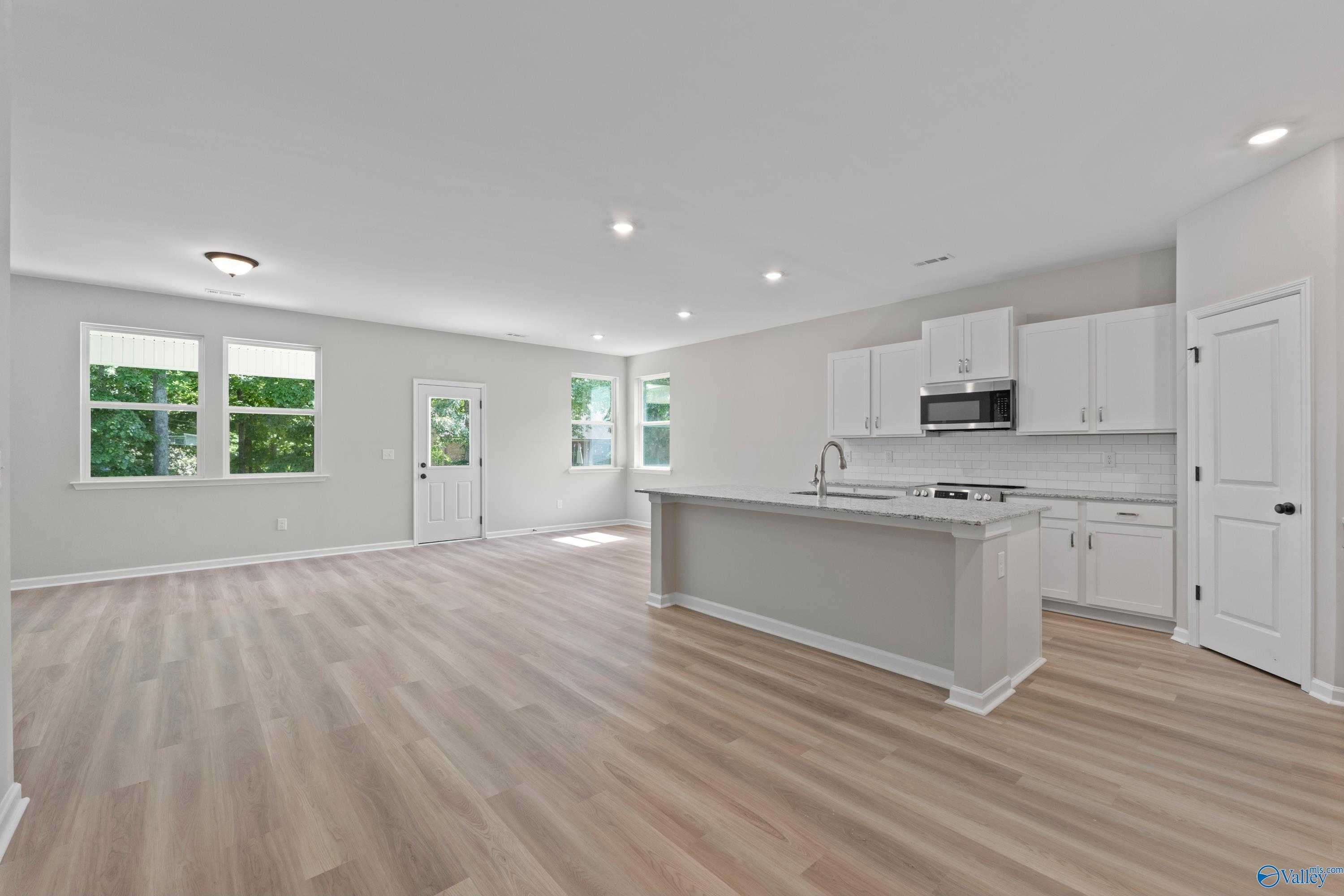 Open-concept kitchen with white cabinets, stainless microwave, gray island sink, and hardwood floors in Davidson Homes The Phoenix, Fayetteville, TN