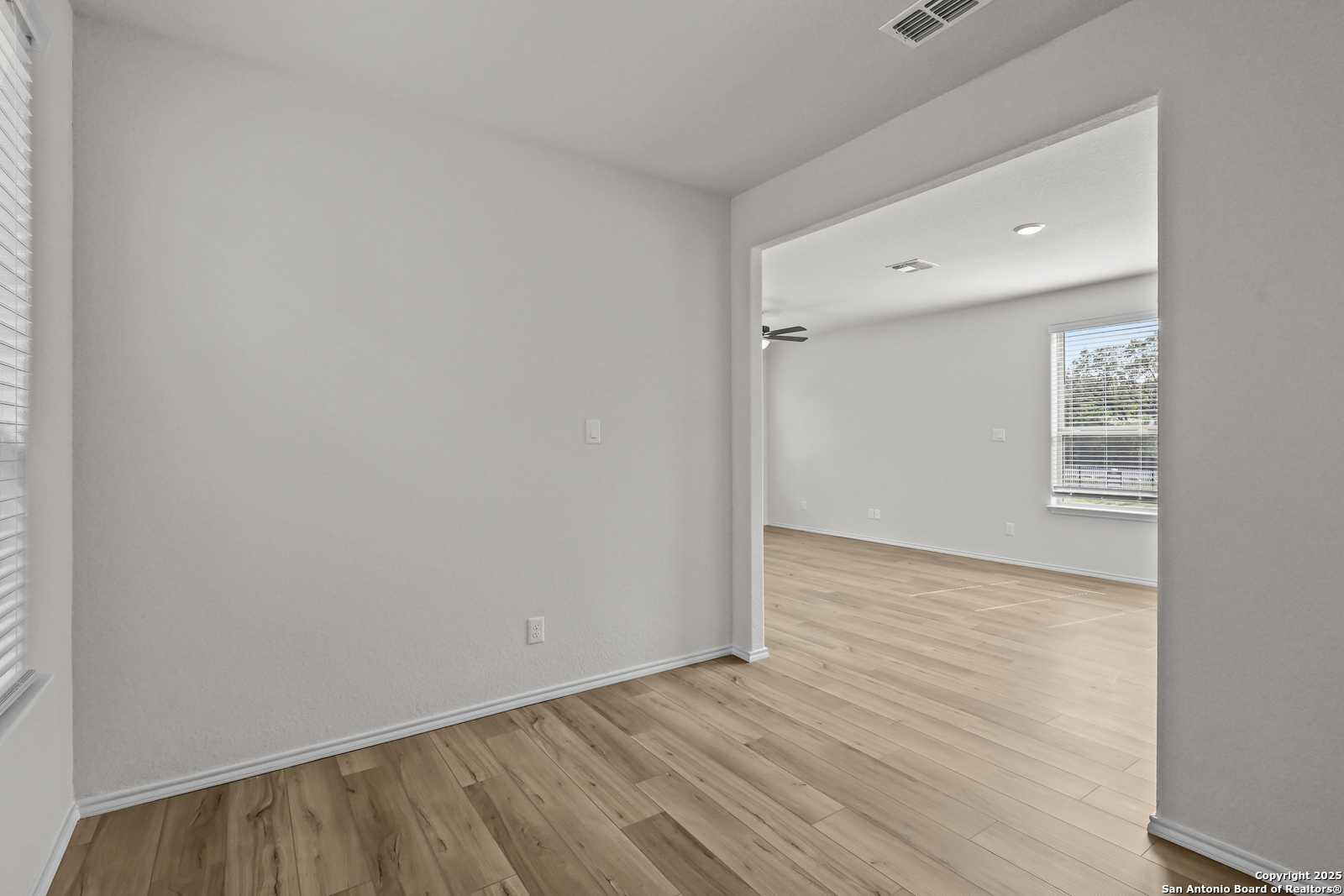 Empty bedroom with light gray walls, hardwood floors, ceiling fan, and window in Davidson Homes The Florence C, San Antonio, Texas