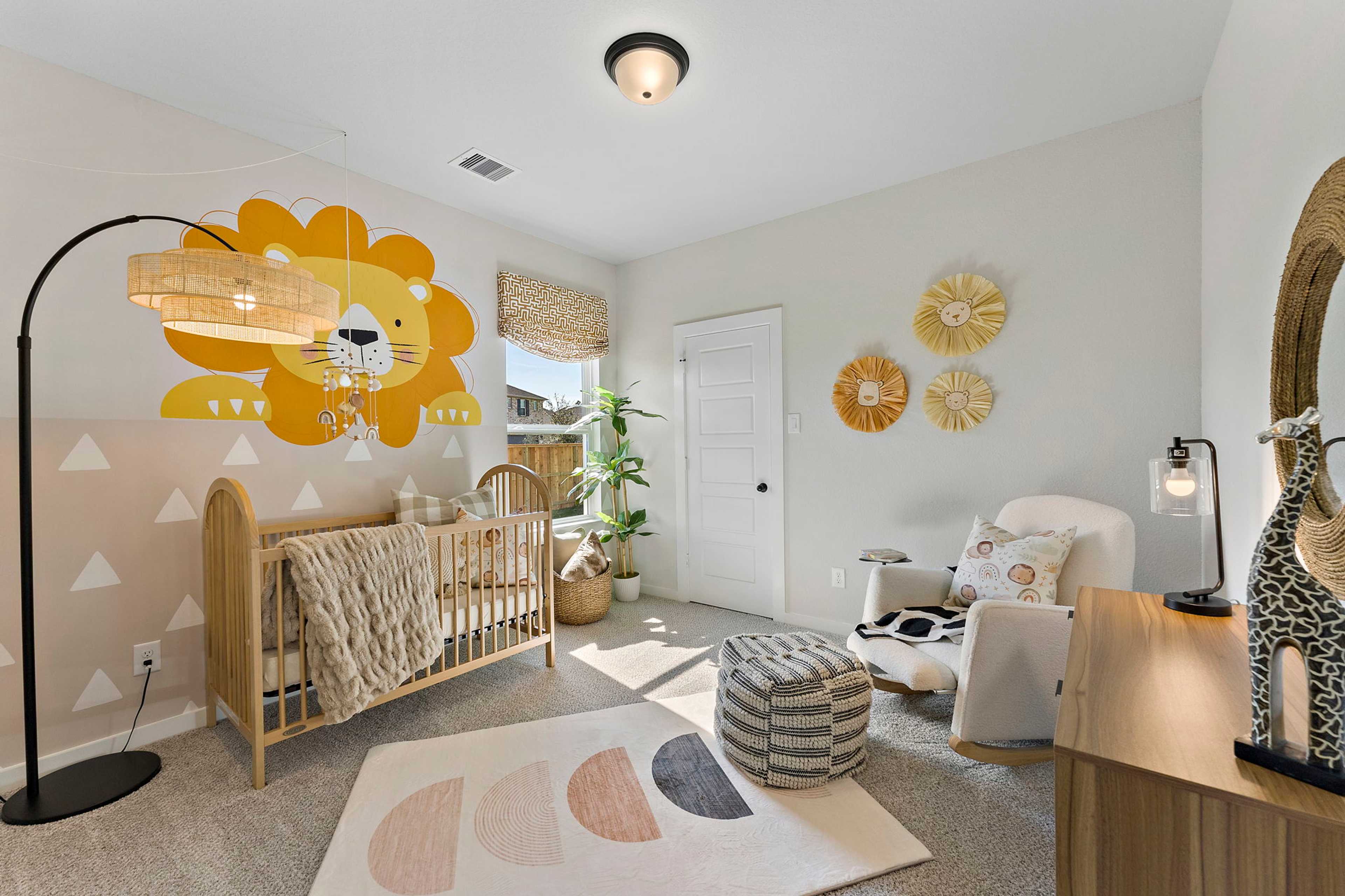Cozy nursery in Sundance Cove Crosby TX with yellow lion wall decal, wooden crib, rattan accents and giraffe decor
