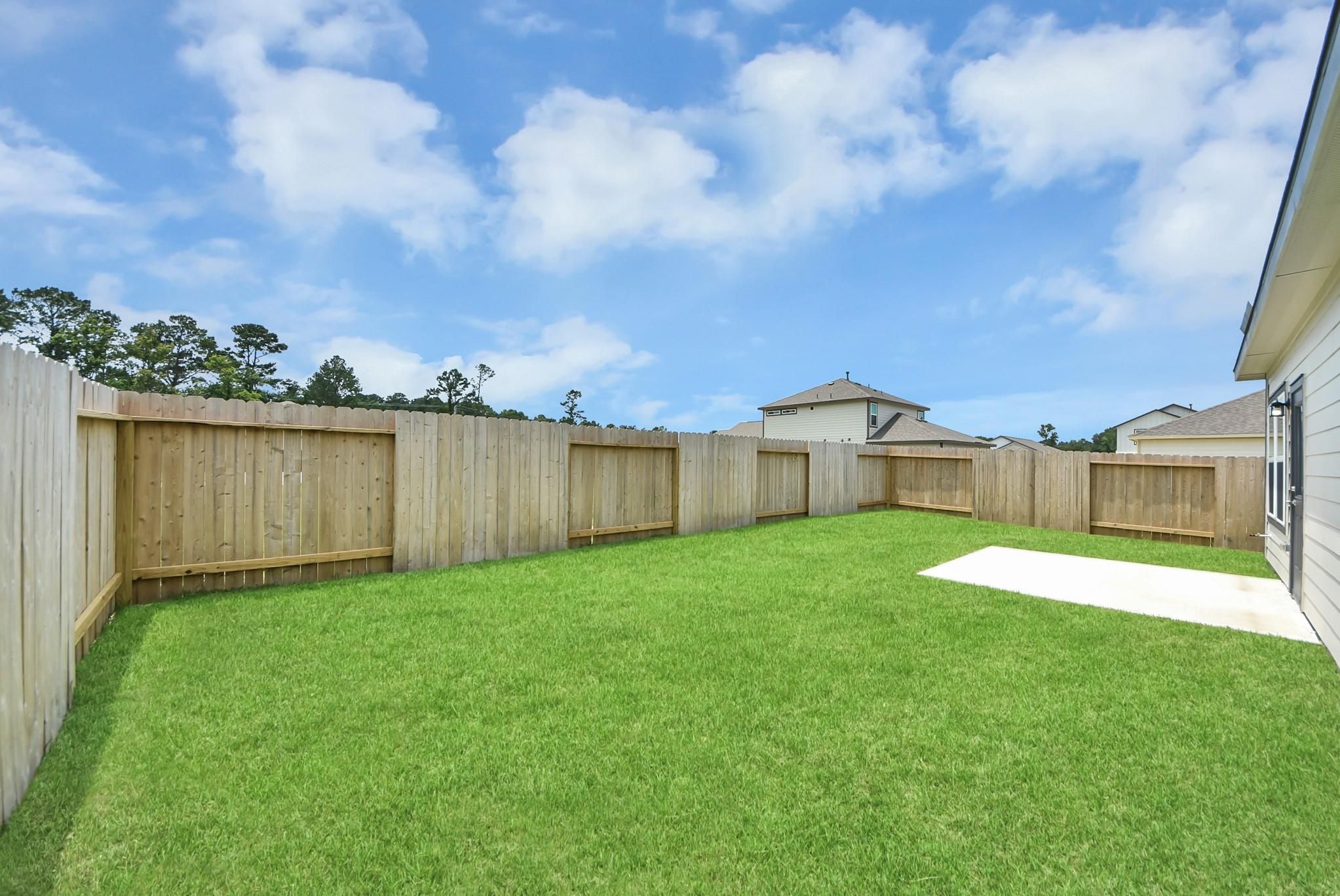 Private fenced backyard with grass lawn and concrete patio at The Blanco E home in The Villages at WestPointe, Dayton, TX.