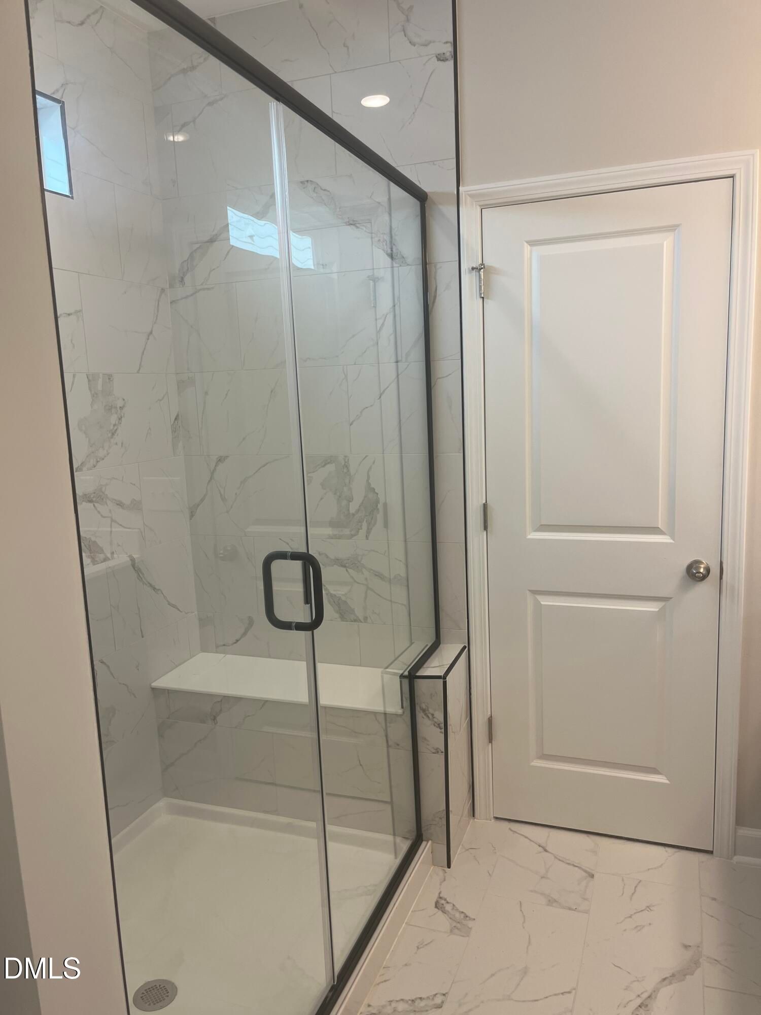 Modern frameless glass shower with marble subway tiles and built-in bench in primary bathroom, The Ashport L by Davidson Homes, Wake Forest NC