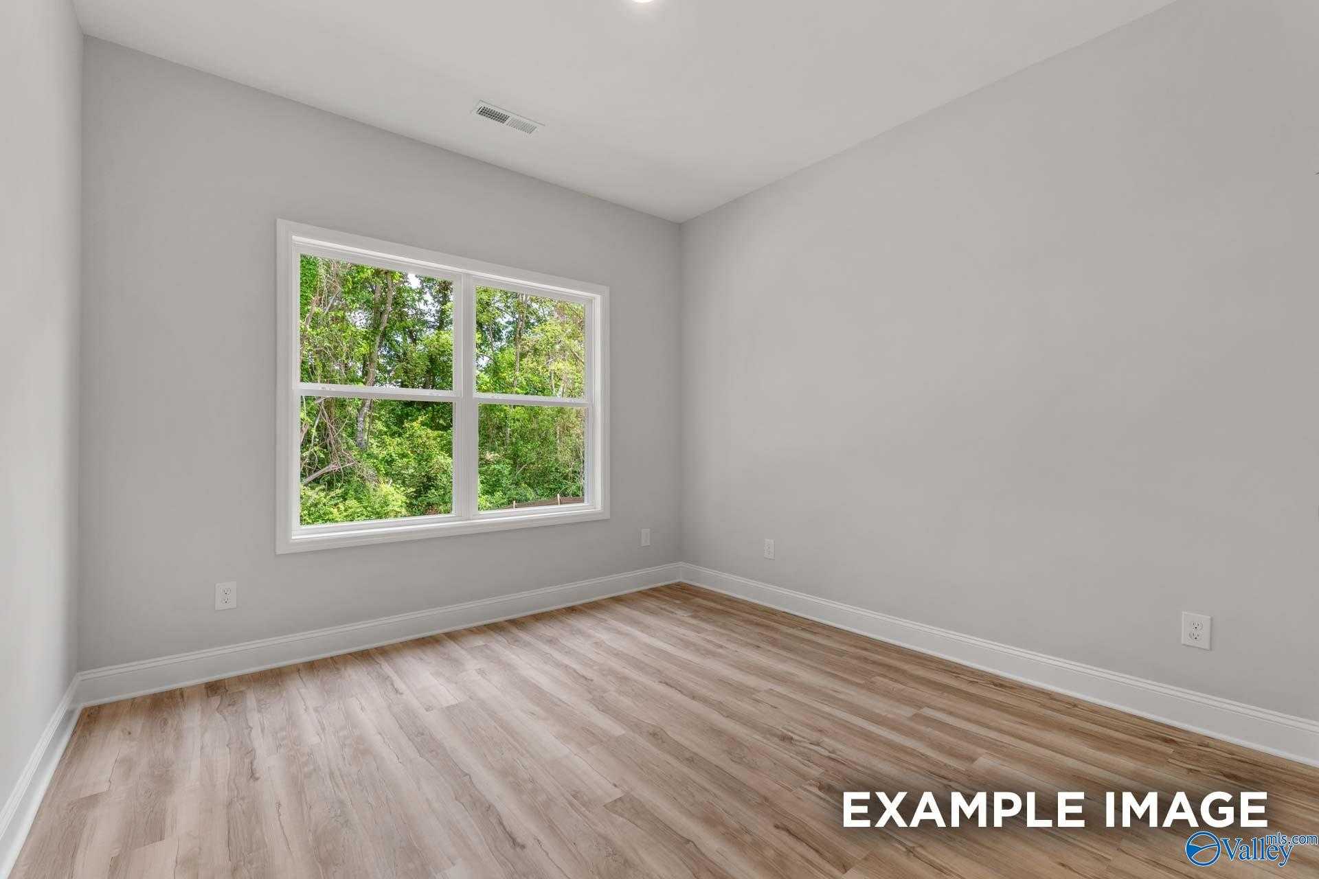 Bright secondary bedroom with hardwood floors, light gray walls, and large window overlooking lush greenery in Davidson Homes The Shelby C, Meridianville, Alabama