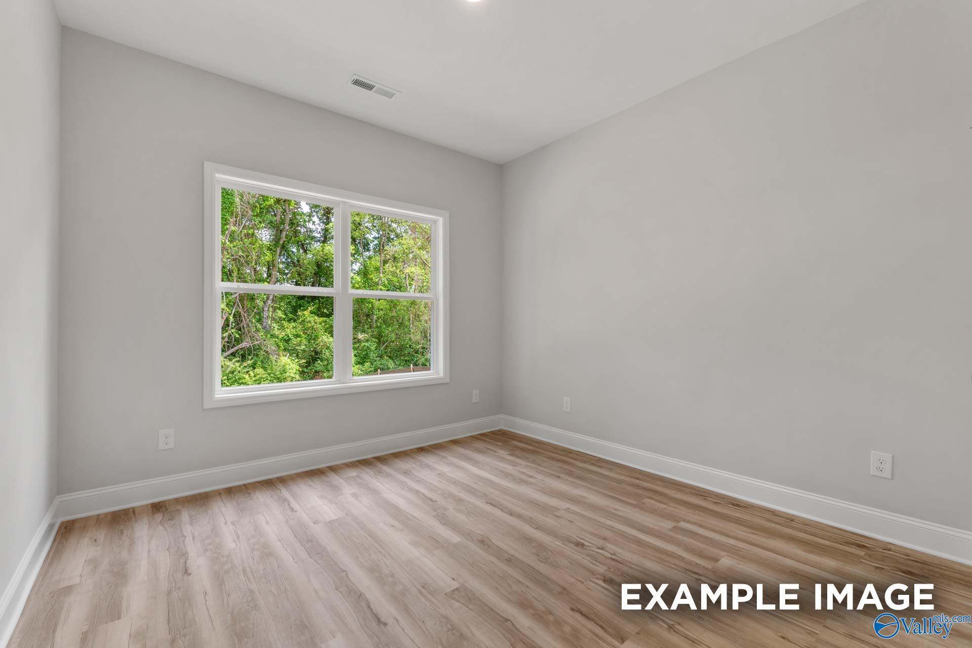 Bright secondary bedroom with hardwood floors, light gray walls, and large window overlooking lush greenery in Davidson Homes The Shelby C, Meridianville, Alabama