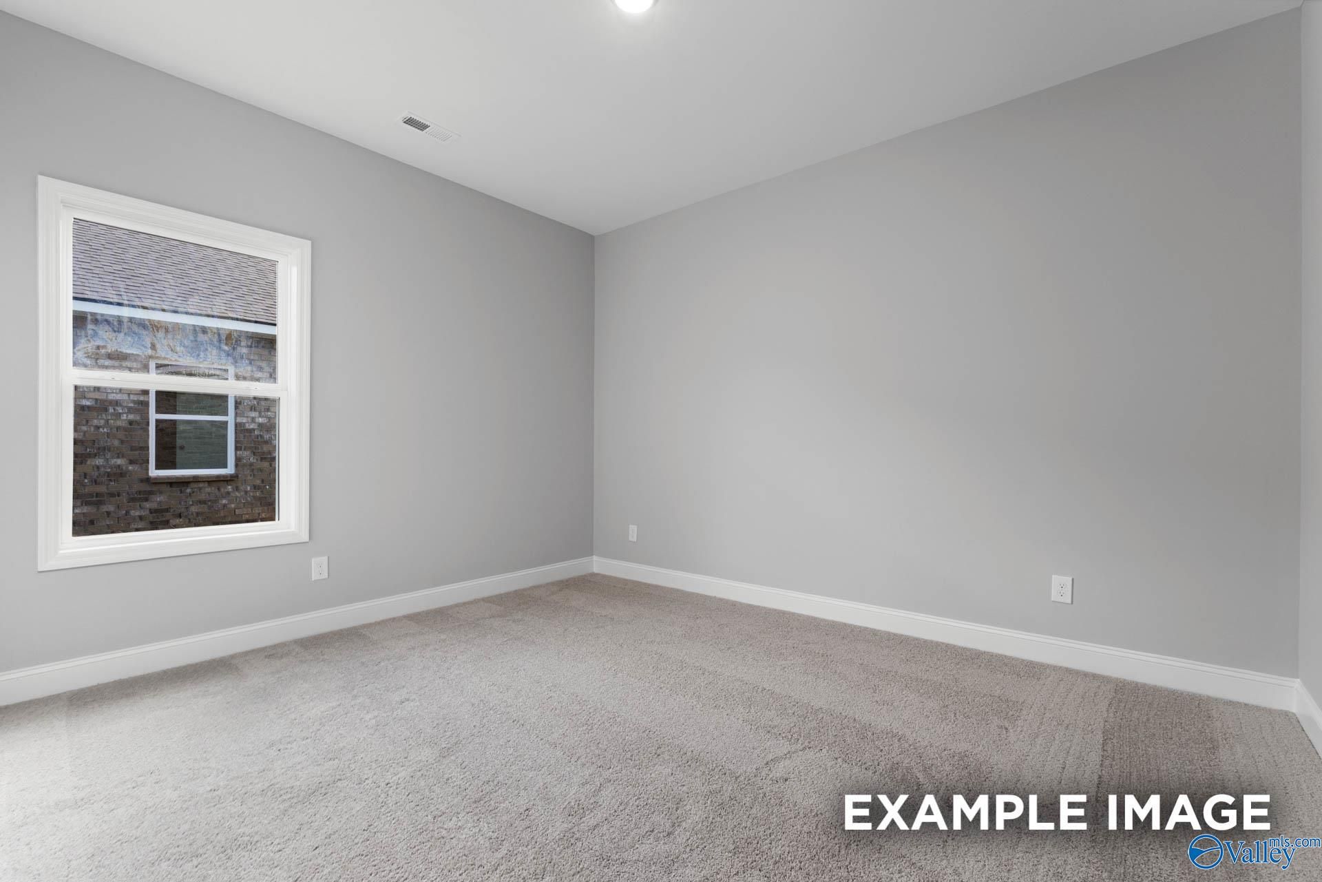 Bright secondary bedroom with large window, neutral gray walls, and carpet floor in The Daphne D floor plan, Meridianville, Alabama