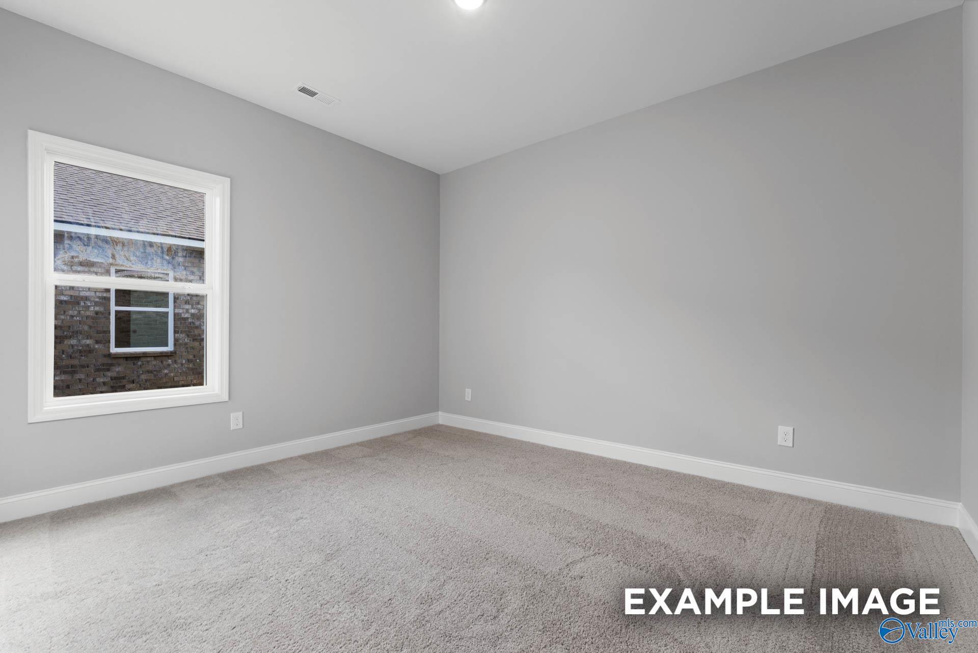Bright secondary bedroom with large window, neutral gray walls, and carpet floor in The Daphne D floor plan, Meridianville, Alabama