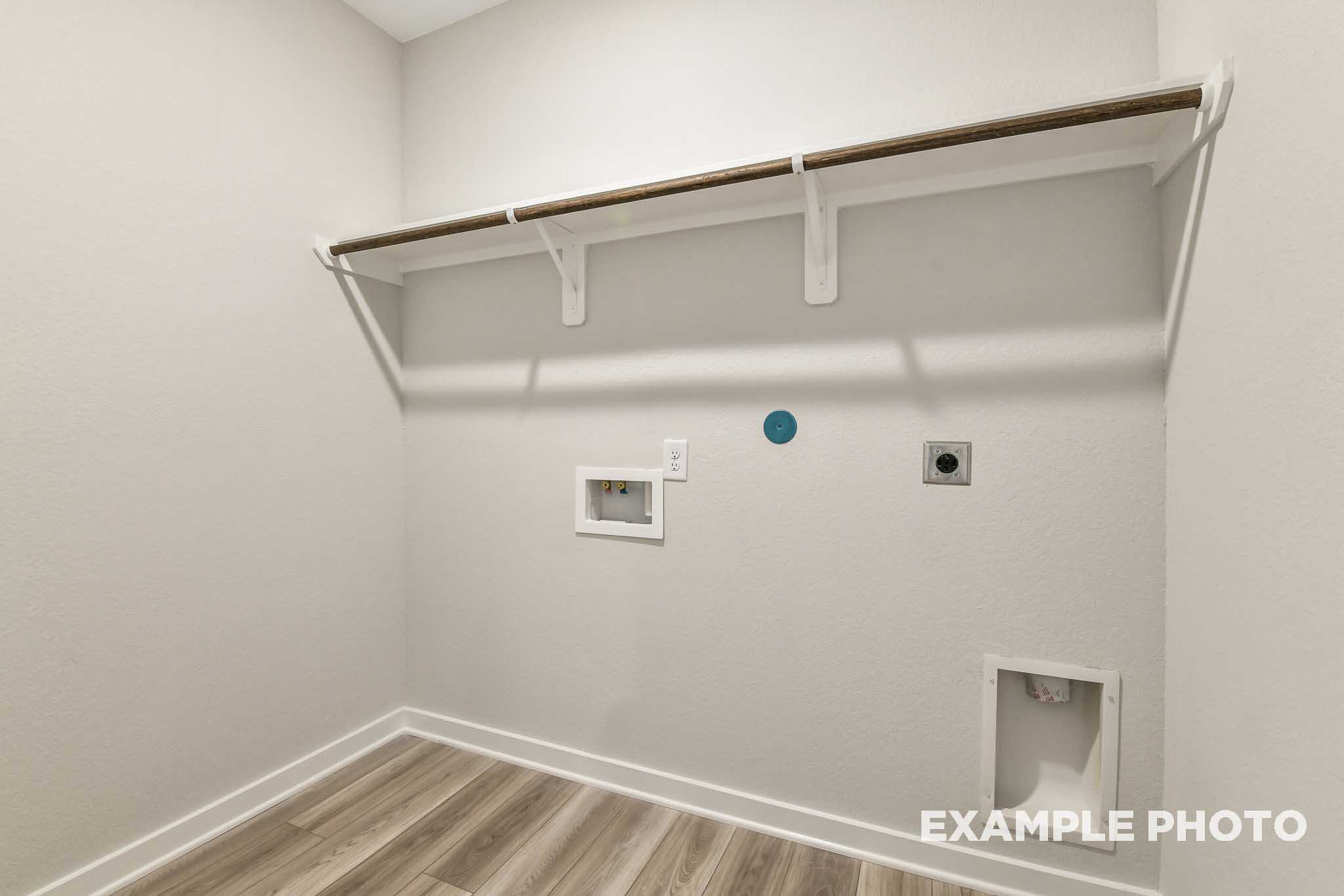 Spacious laundry room in The Daphne G with built-in wooden shelves, washer dryer hookups, and light wood flooring