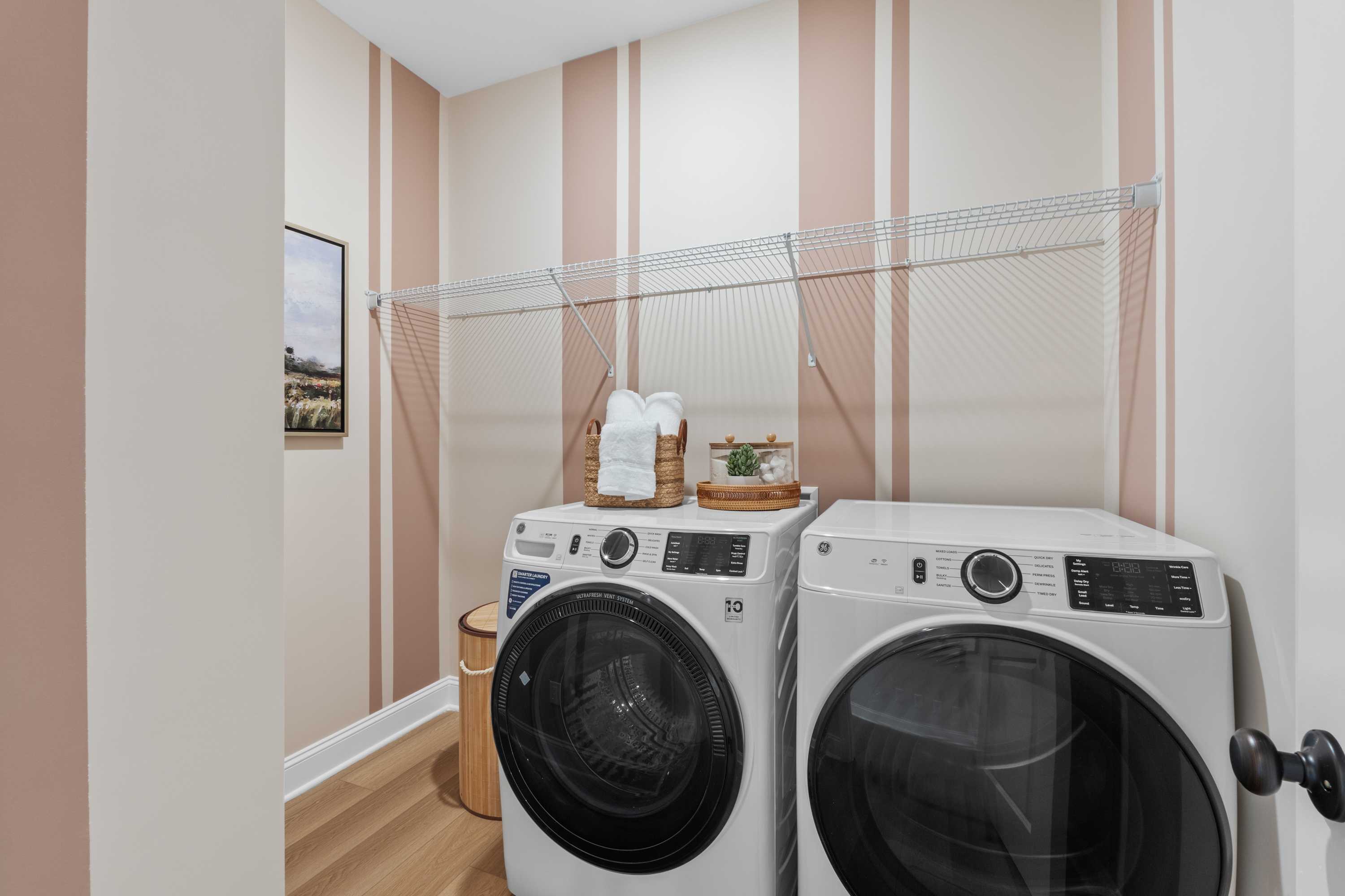 Modern laundry room in The Daphne F with white side-by-side washer dryer, pink-striped beige walls, hardwood floors