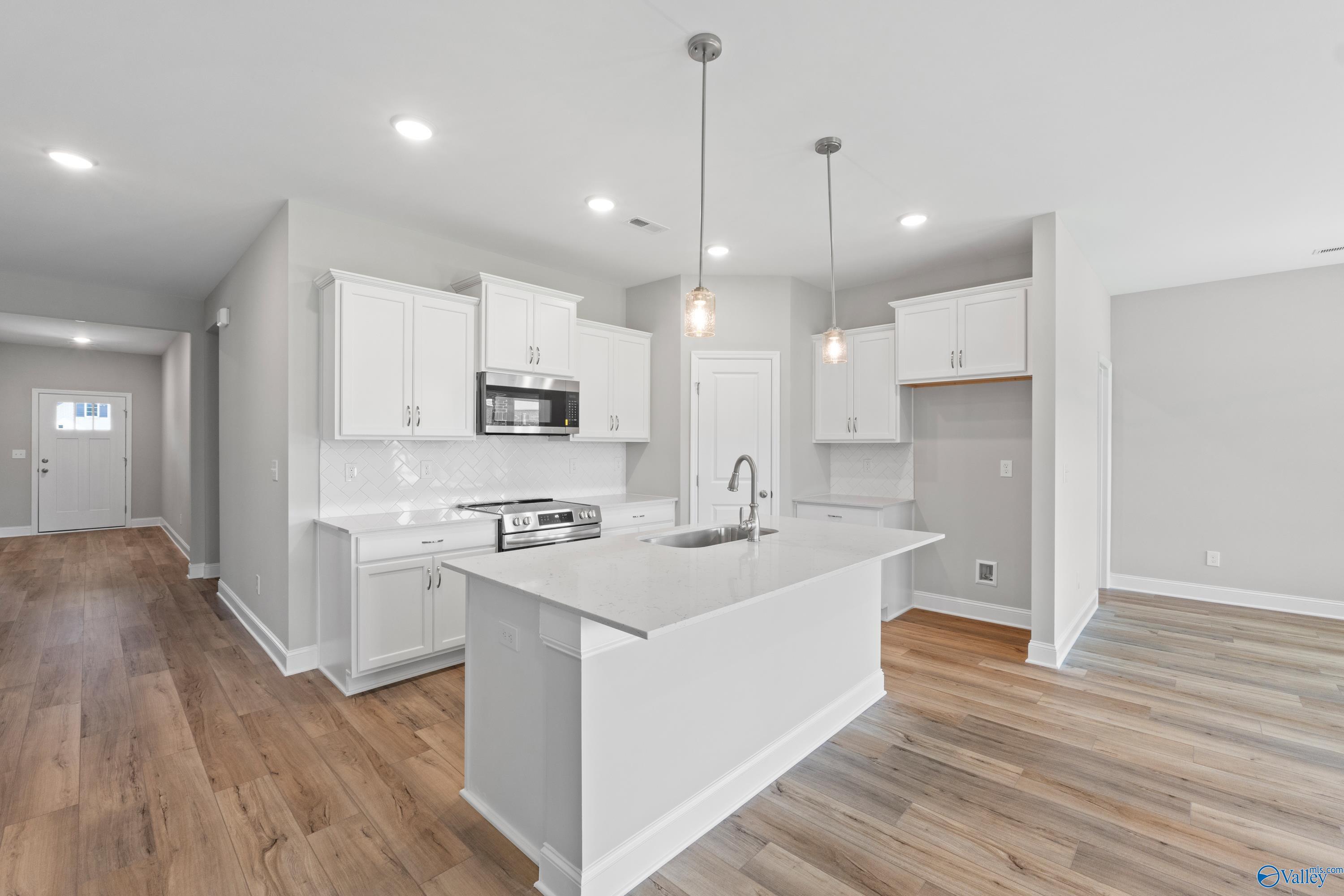 Modern white kitchen with quartz island, stainless appliances, pendant lights in 4-bedroom Davidson Homes The Daphne C, Athens AL