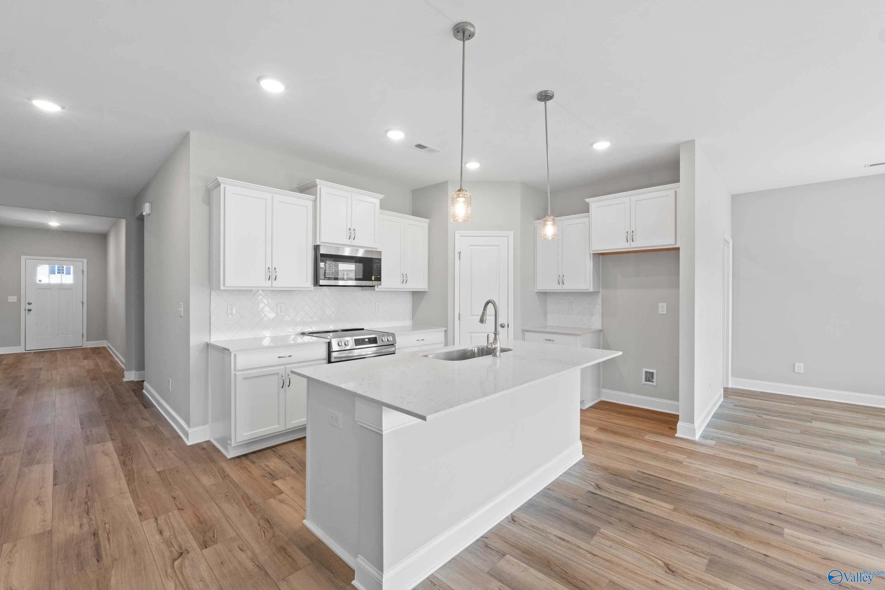 Modern white kitchen with quartz island sink, stainless appliances, and hardwood floors in Davidson Homes The Daphne C, Athens AL