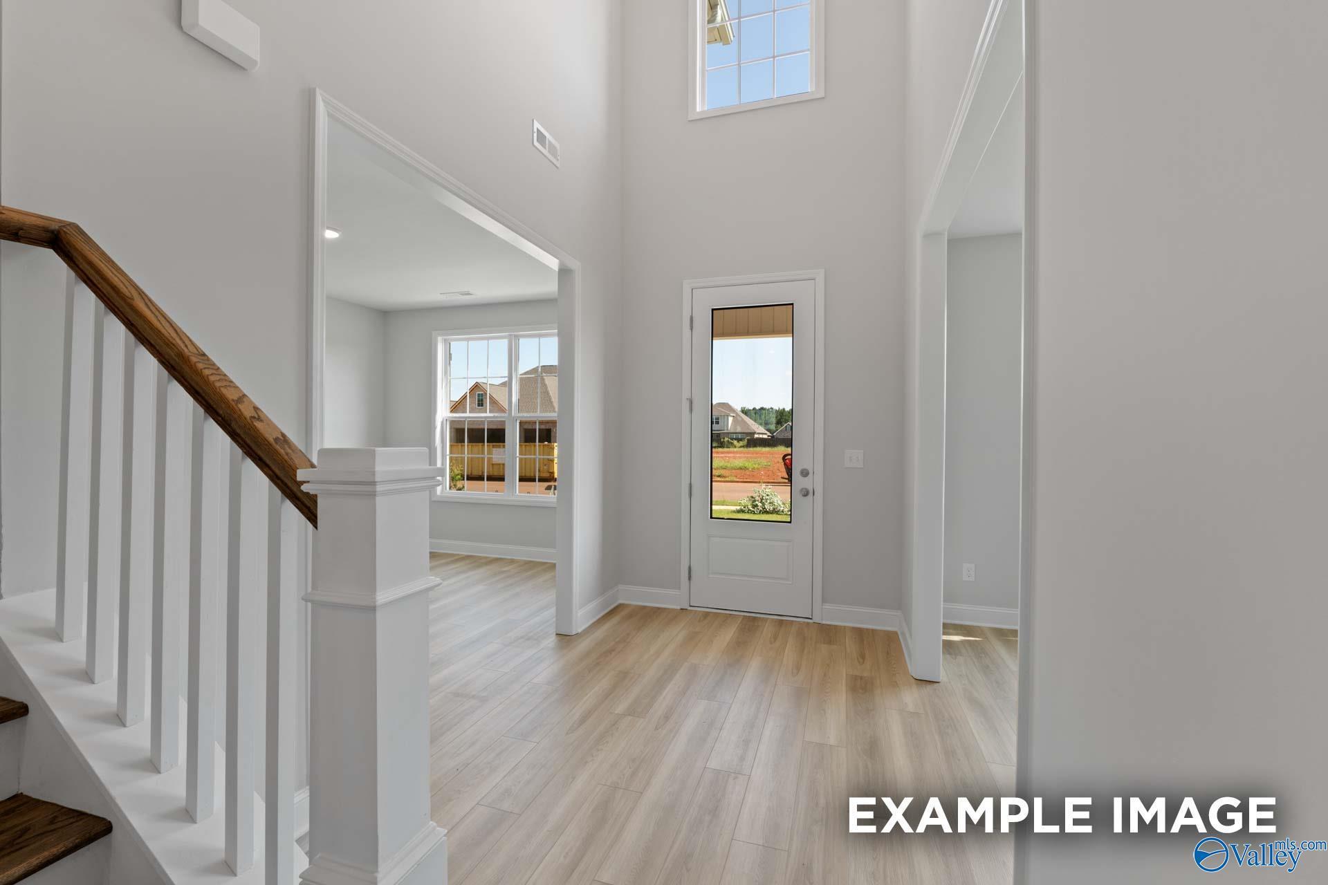Spacious entry foyer with wooden staircase, white balusters, light oak floors, and glass door to backyard in The Madison A, Toney Alabama