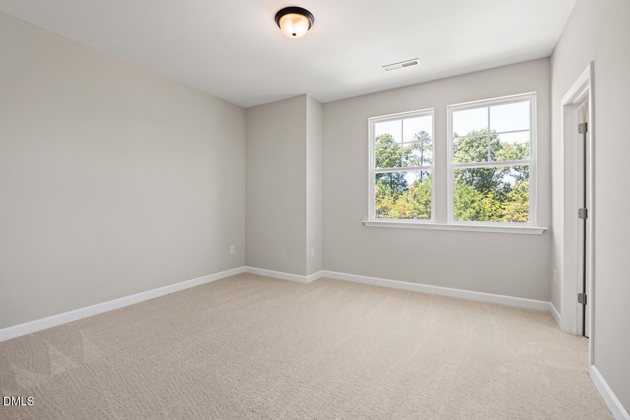 Bright, carpeted bedroom with neutral walls and large windows in The Chestnut floor plan at Montrose, Aberdeen, NC.
