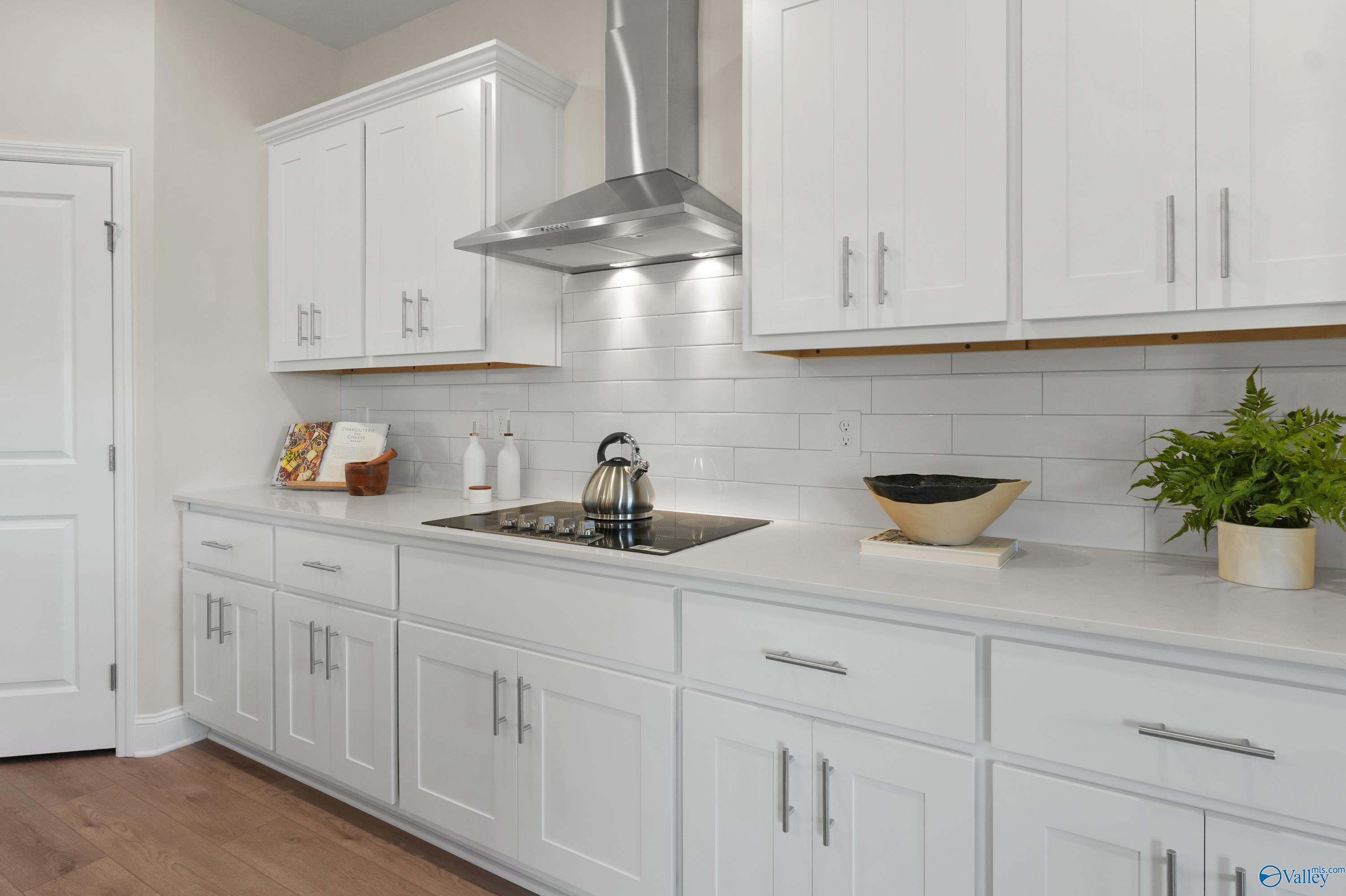 Bright white kitchen with shaker cabinets, stainless range hood, cooktop, and subway tile backsplash in Davidson Homes The Rockford B, Toney, Alabama