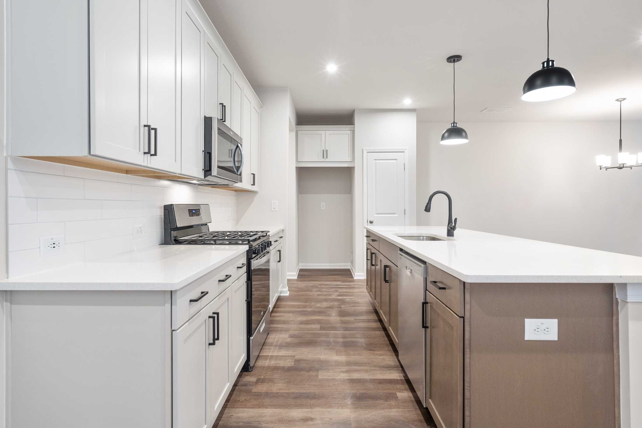 Modern kitchen in The Cary B with white shaker cabinets, stainless steel appliances, large quartz island, and subway tile backsplash