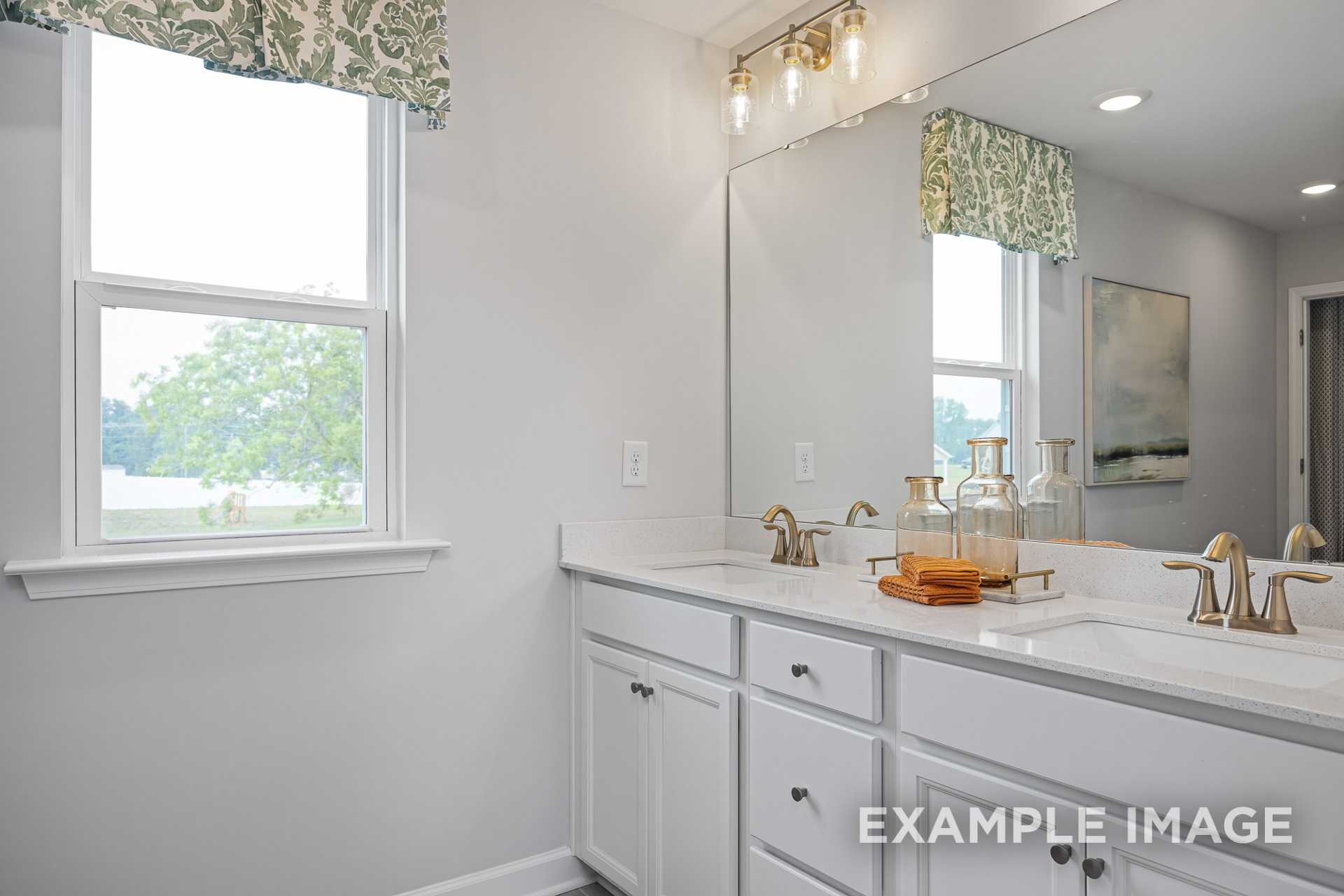 Spacious master bathroom in The Adalynn A featuring double white vanity, mirrors, pendant lights, and window with tree view