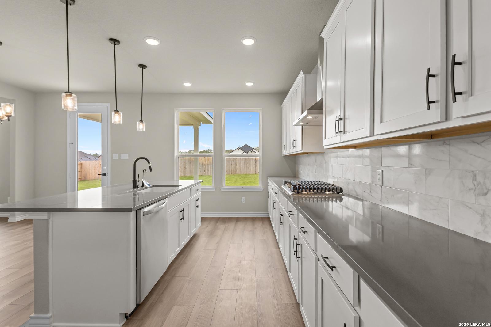Modern kitchen with white cabinets, quartz countertops, and pendant lighting in The Danbury H floor plan, Castroville, TX.